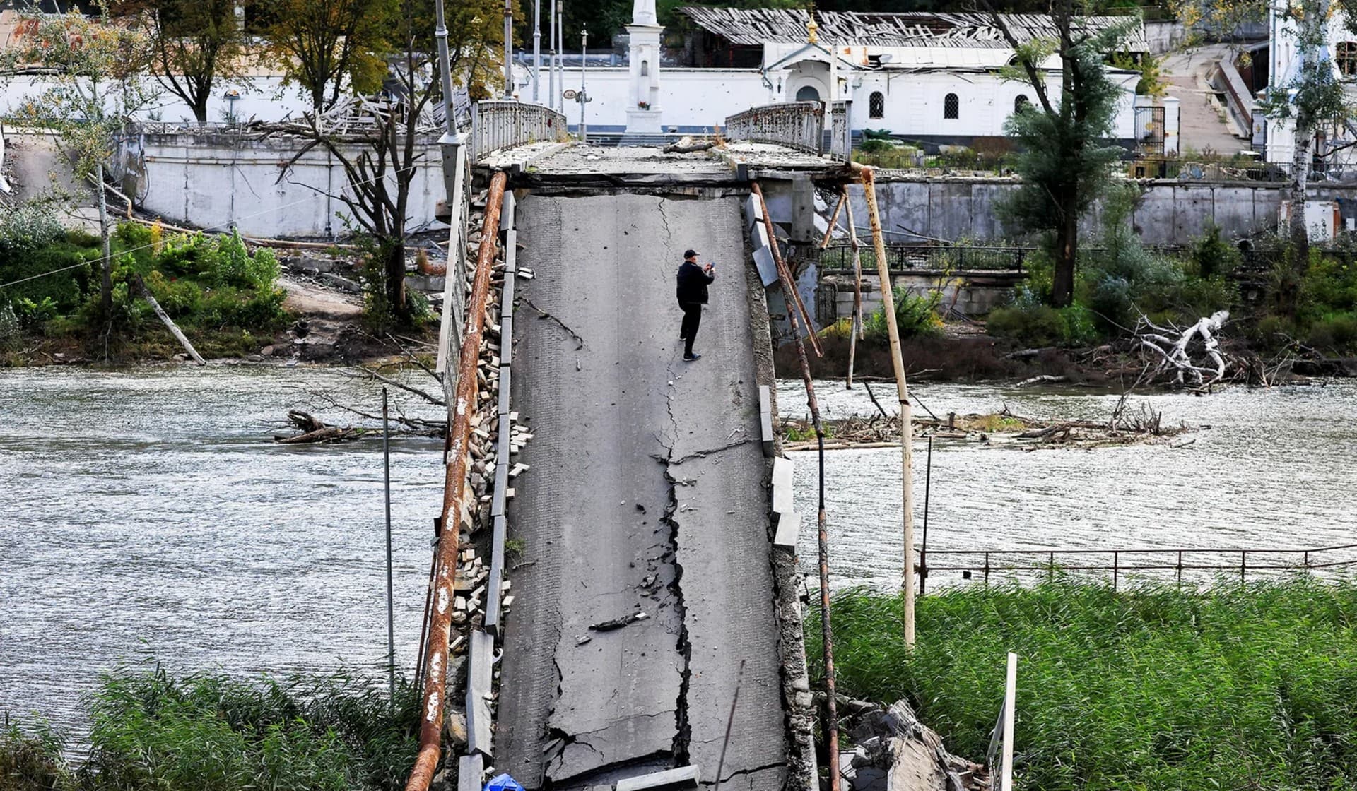 A man uses his mobile phone as he stands on a bridge destroyed by a Russian missile strike in Svyatohirsk