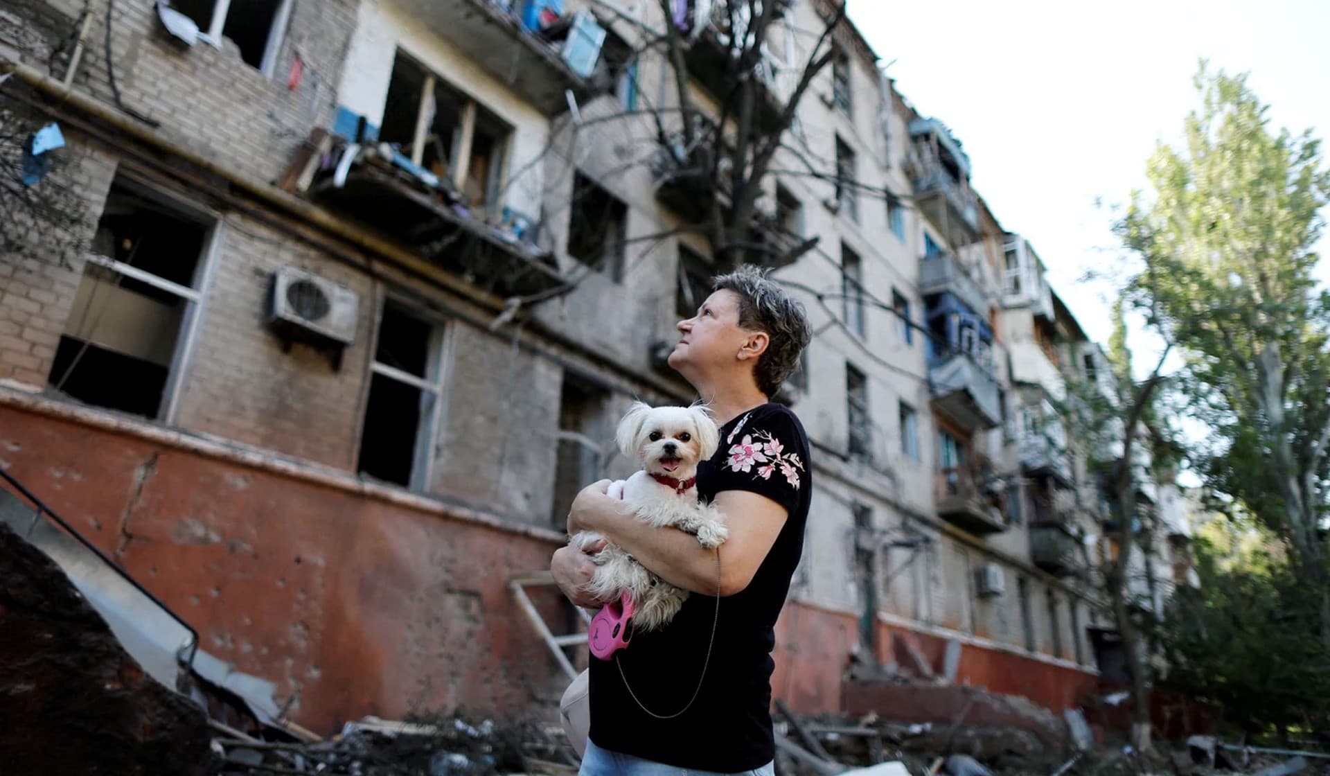 A Ukrainian woman holds a dog as she looks at a residential building damaged after a Russian strike in Kramators