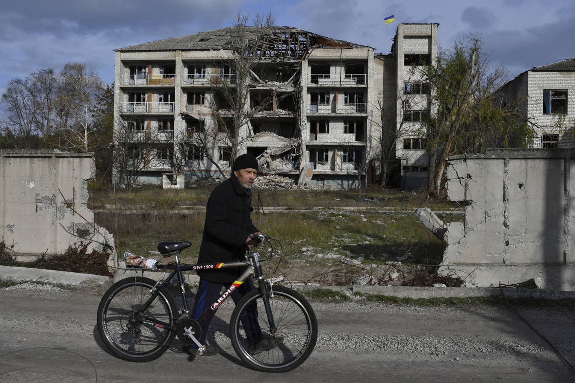 A man with a bicycle passes a building damaged by shellings in the liberated village of Shchurove