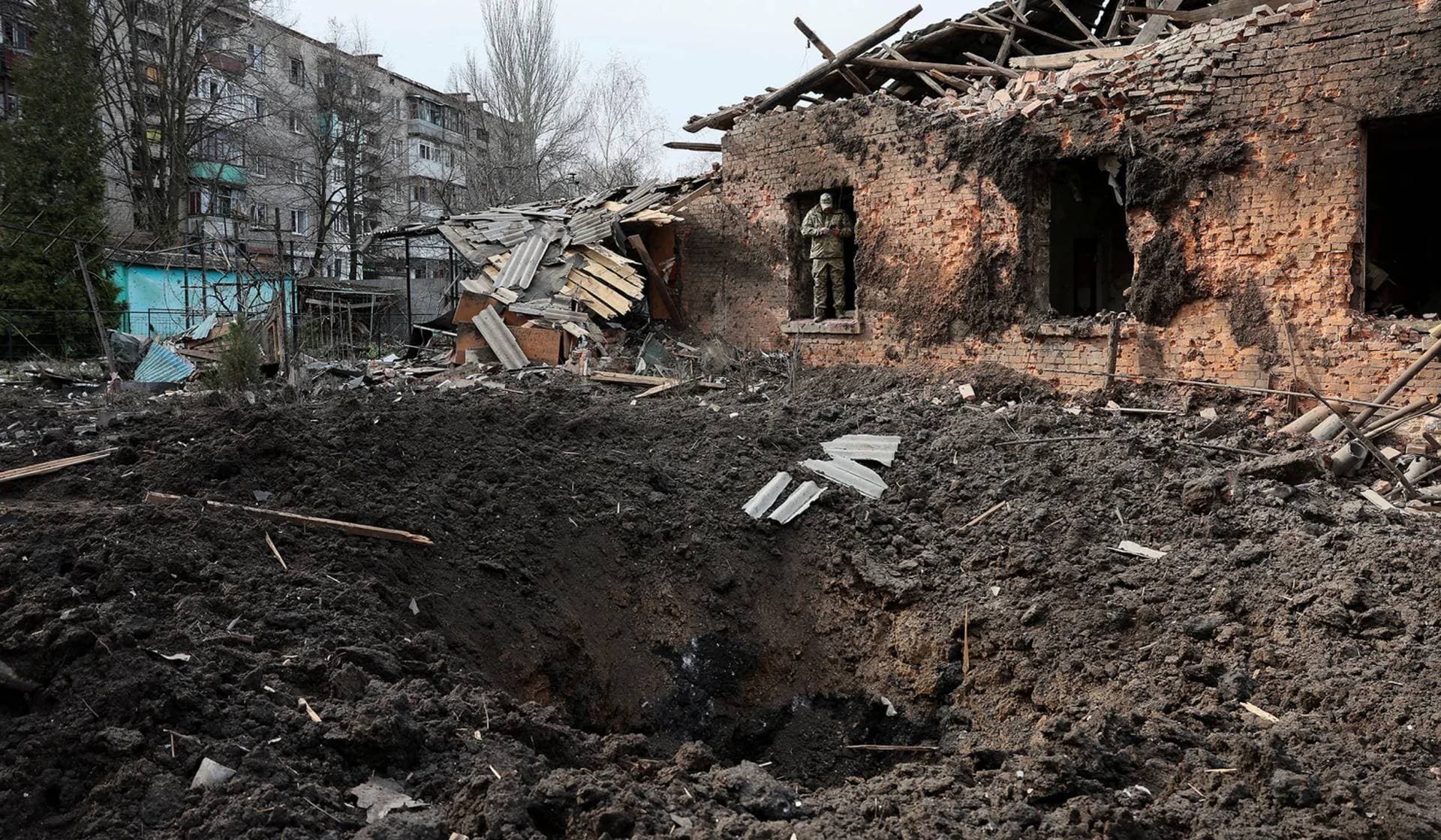 A Ukrainian serviceman uses his phone near a crater in the aftermath of deadly shelling of residential buildings in Kostiantynivka
