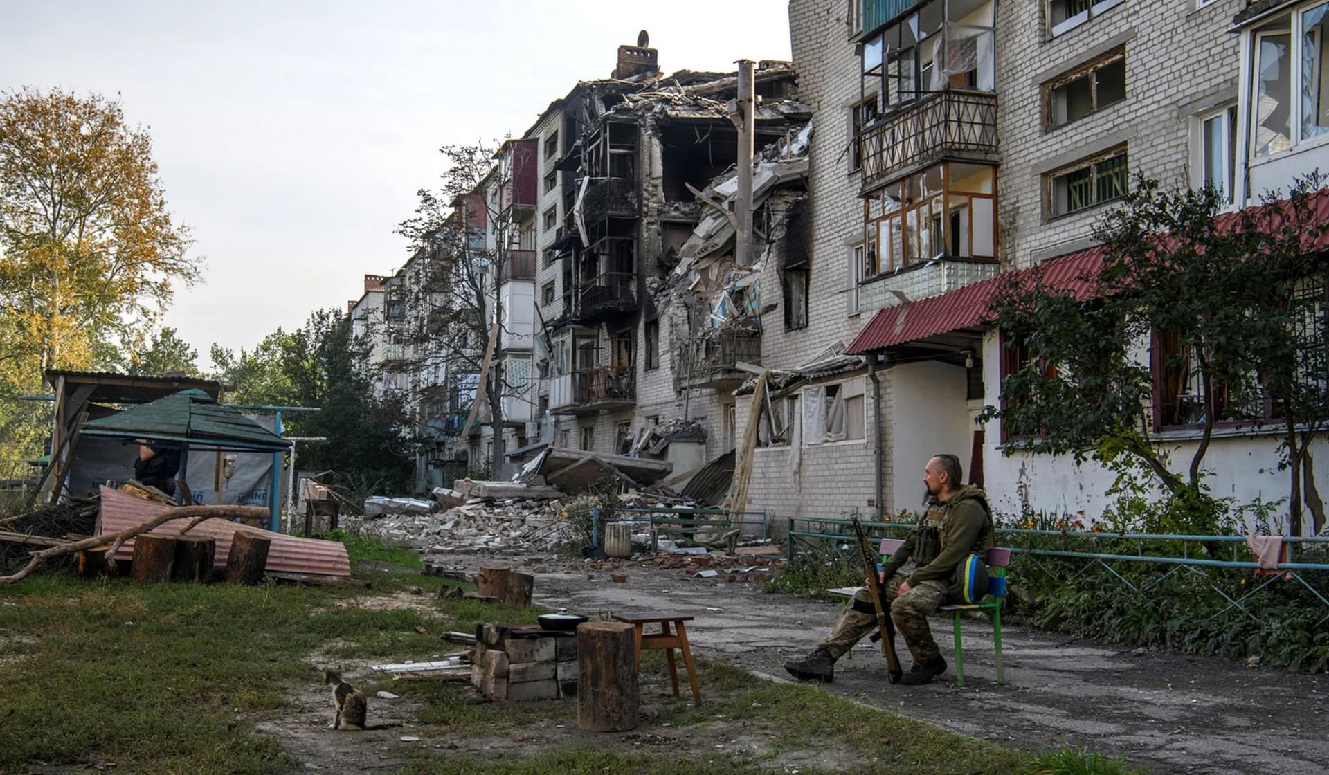 A Ukrainian service member sits on a bench near a destroyed residential building in the town of Sviatohirsk