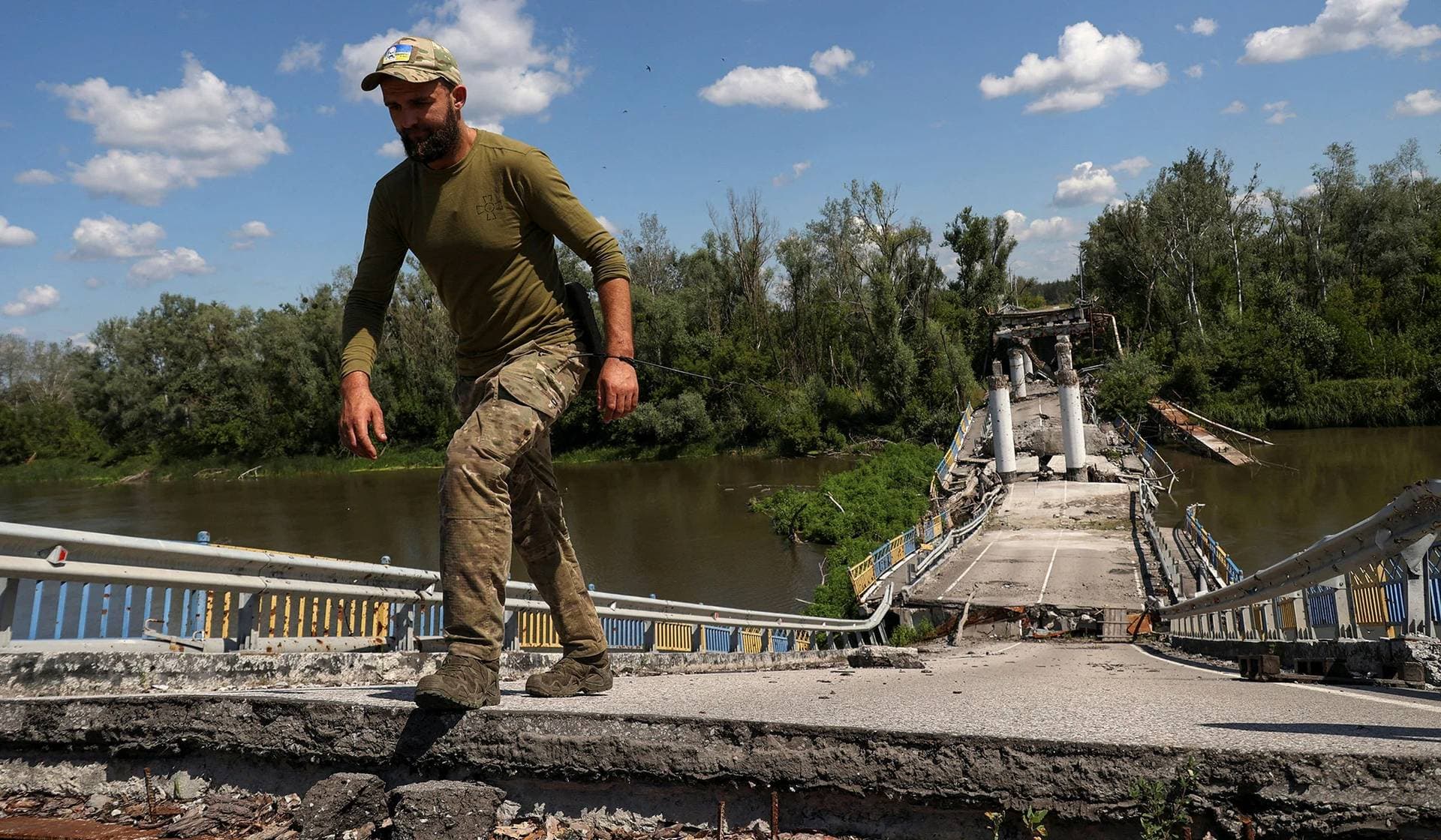 A Ukrainian serviceman walks on a destroyed bridge over the Siverskyi Donets River in the village of Bohorodychne