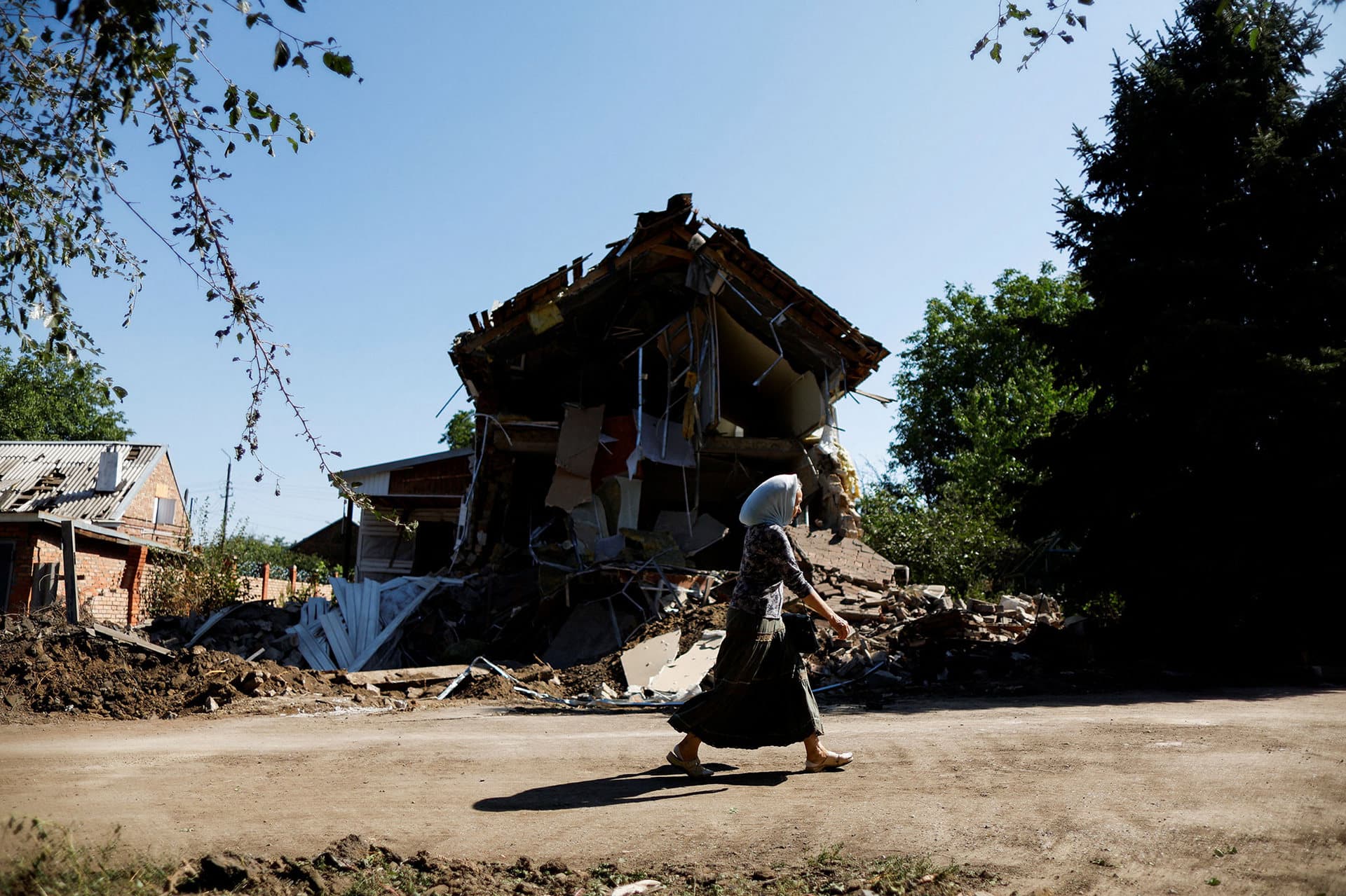 A woman walks near a destroyed house by shelling in Kostyantynivka