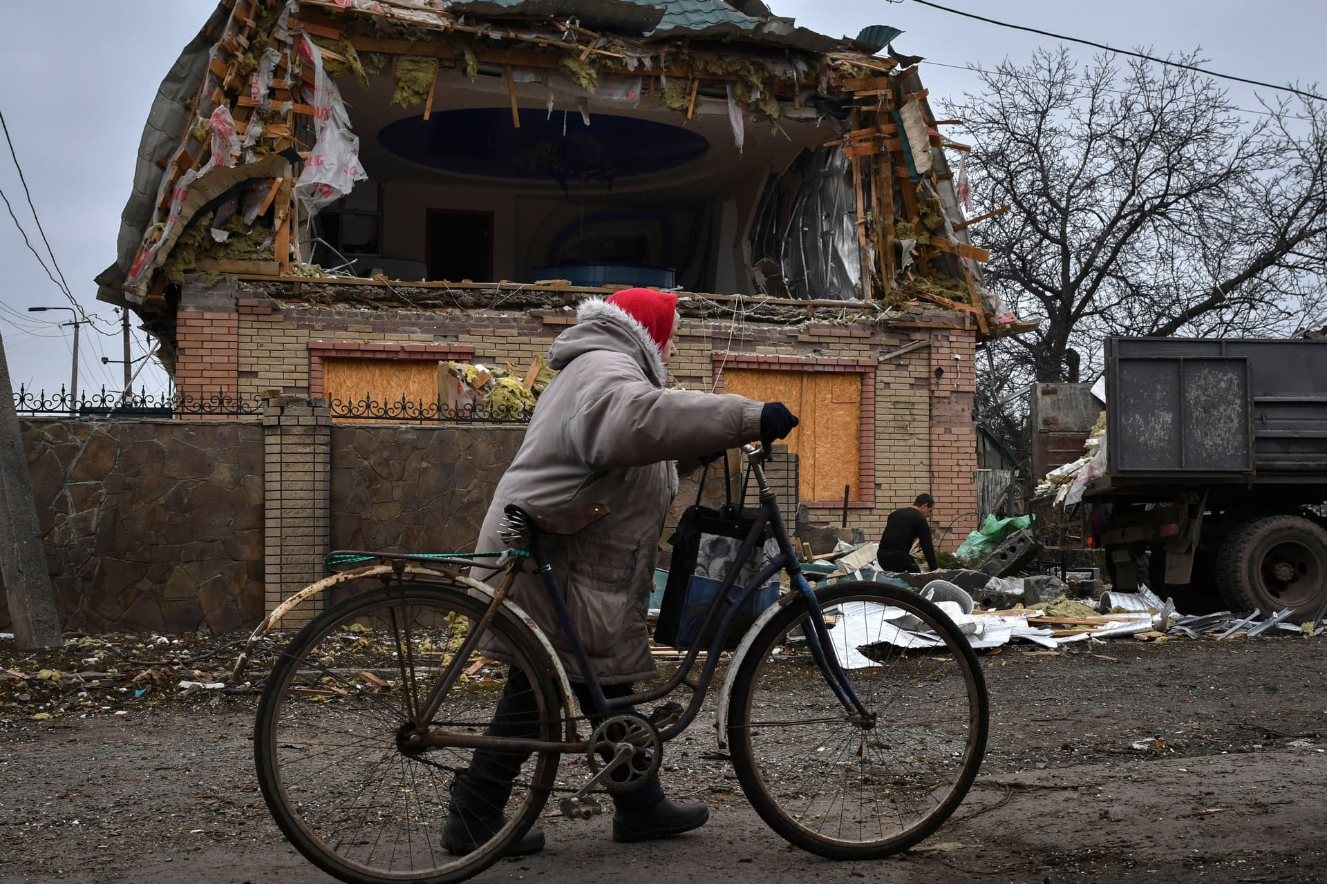 A woman passes with a bicycle as a local resident works to clean the debris from a damaged house after Russian shelling in Kramatorsk