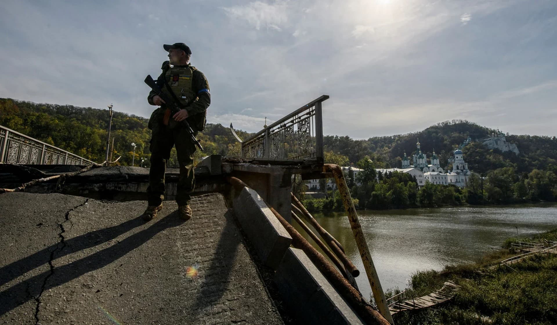 A service member of Ukraine's National Guard stands at a bridge over the Siverskyi Donets River destroyed during Russia's attack on Ukraine in the town of Sviatohirsk