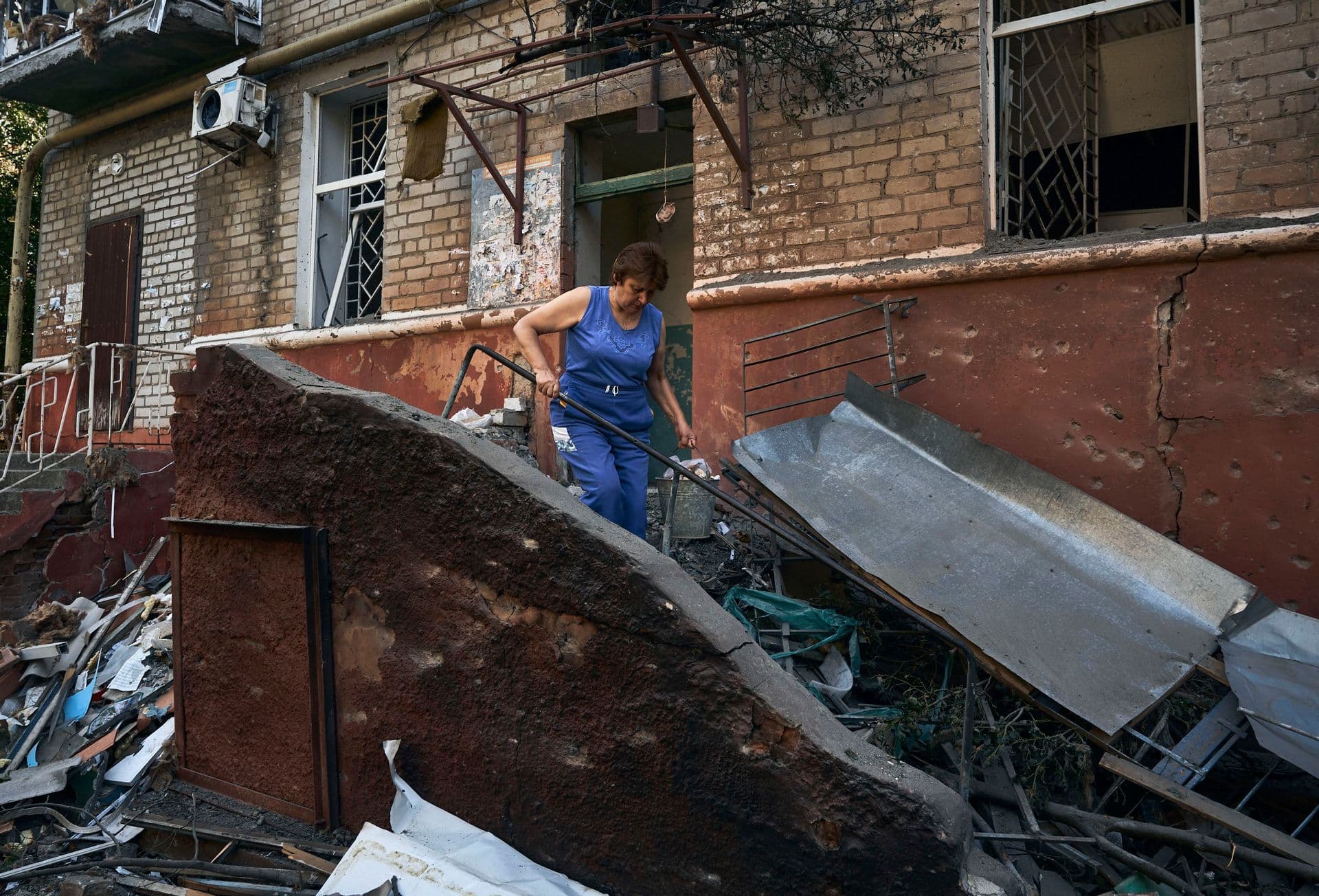 A woman cleans up debris in front of a residential building that was damaged after a Russian rocket attack in Kramatorsk