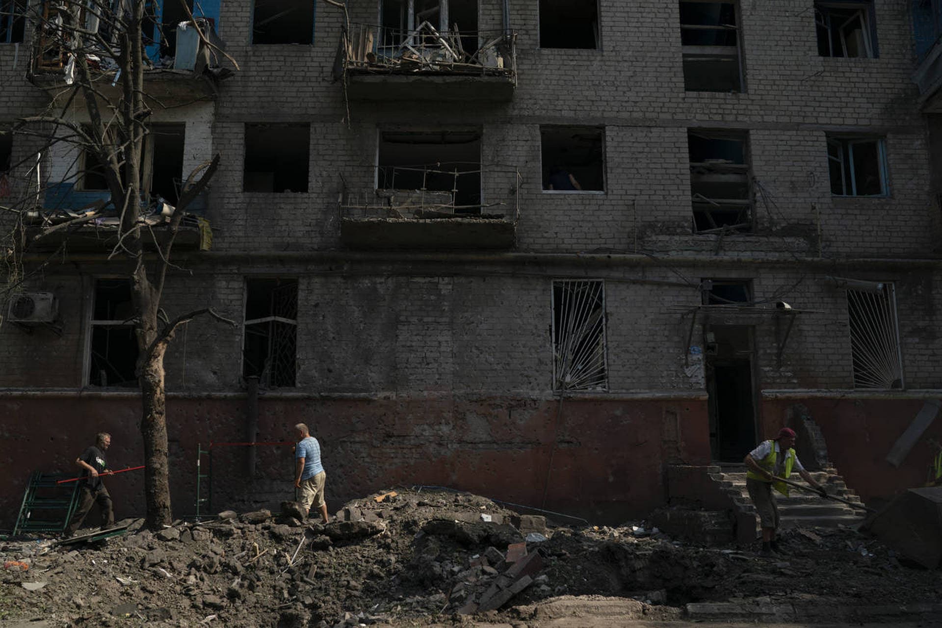 People work to clean up debris in front of a residential building that was damaged after a Russian attack in Kramatorsk