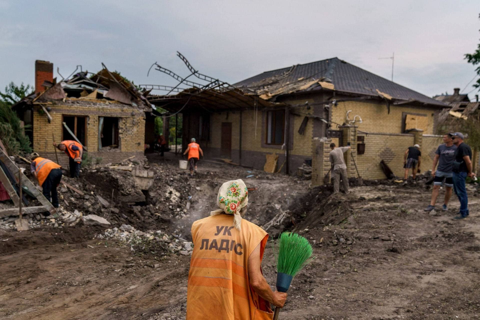 An elderly worker with a broom inspects a crater caused by a rocket strike on a house in Kramatorsk
