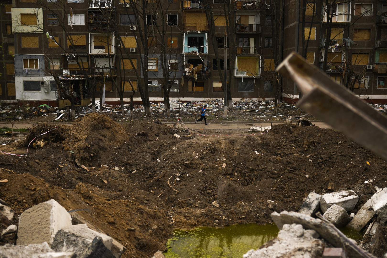 A young local resident passes by a crater caused by a Russian strike earlier in May opposite an apartment building in Kramatorsk