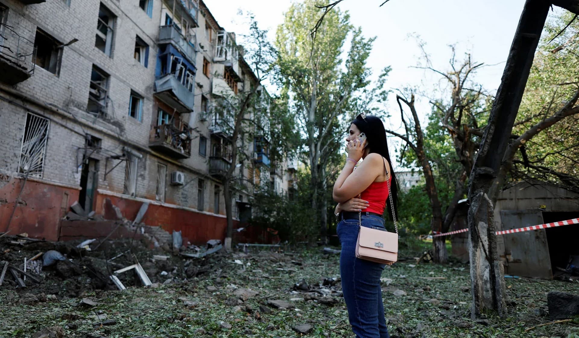 A Ukrainian woman uses her mobile phone in front of a residential building damaged after a Russian strike in Kramatorsk