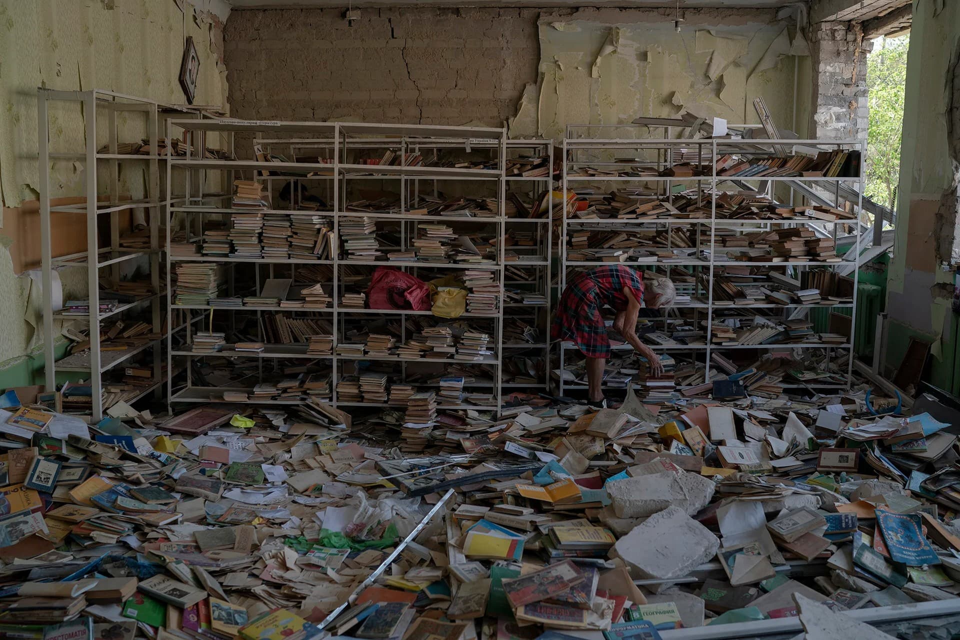 The librarian Raisa Krupchenko makes a pile of books as she tries to organize them among debris at the library of the destroyed School Number 23 in Kramatorsk