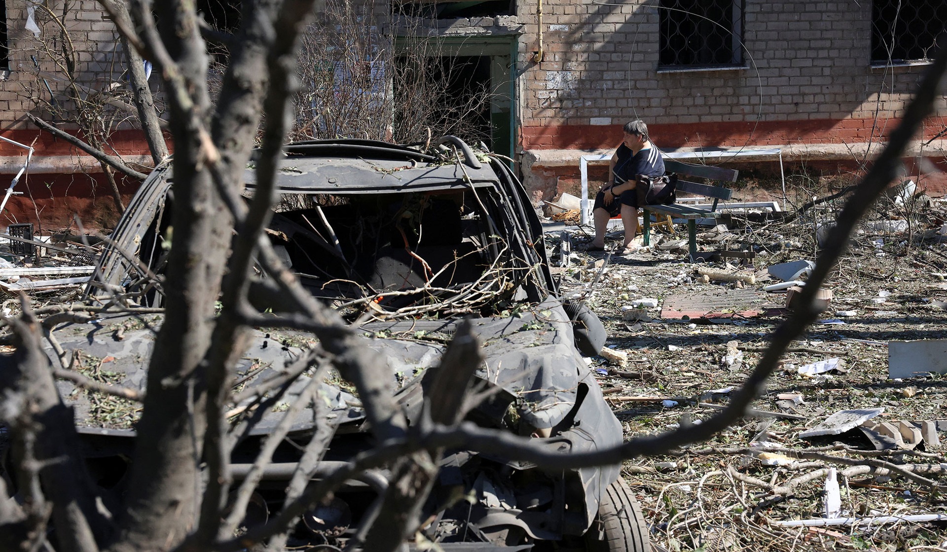 A resident sits on a bench in front of an apartment building damaged during a Russian air strike in the frontline city of Kramatorsk