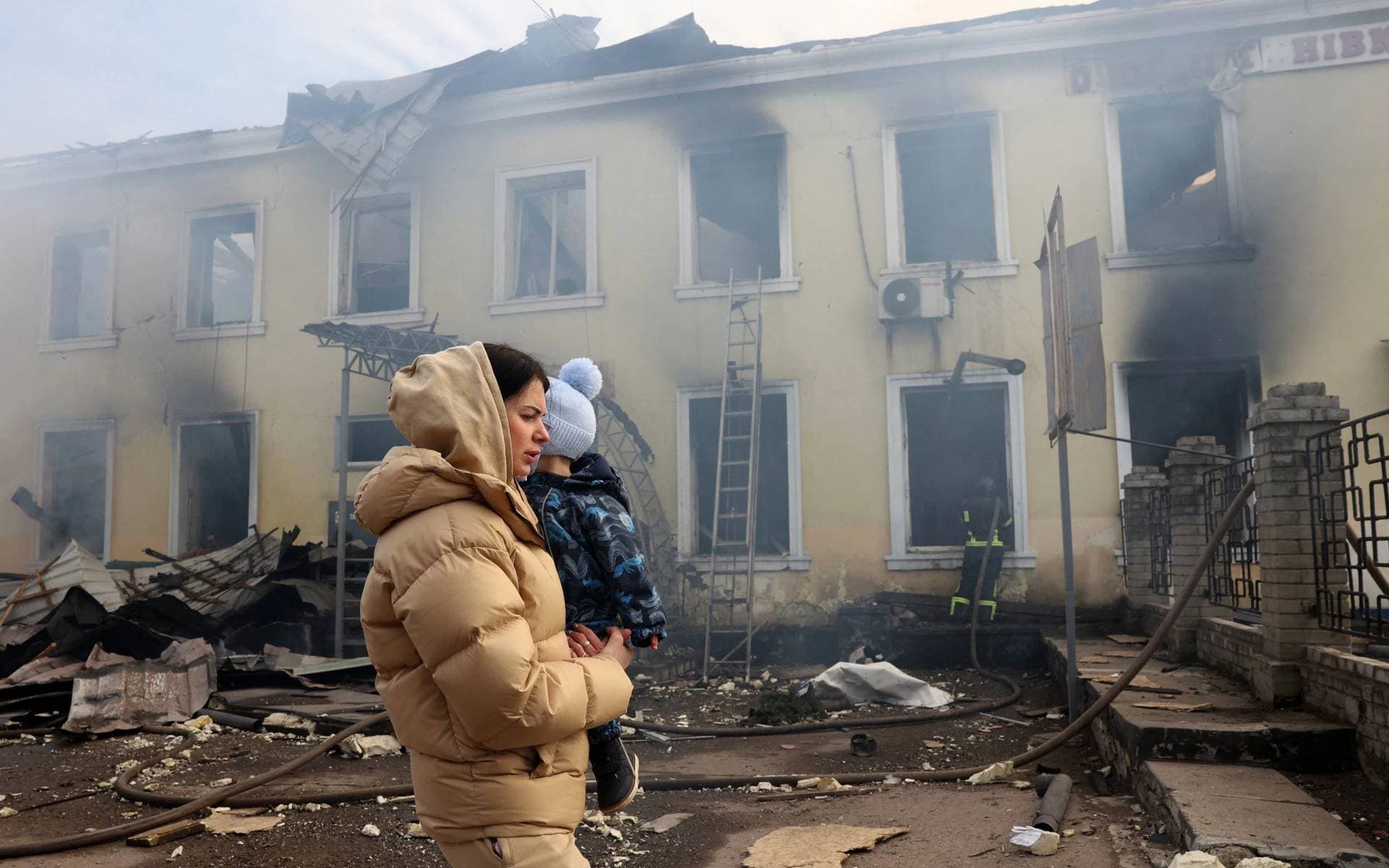 A local resident and her child walks past the railway station destroyed by a Russian missile attack in Konstyantynivka
