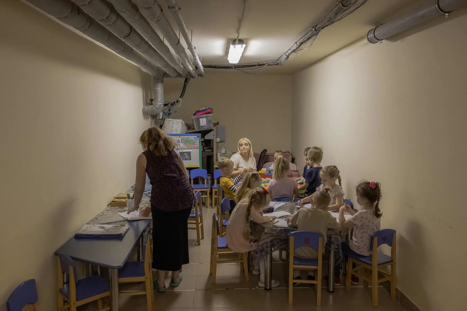 Children and their teachers wait in the basement of a kindergarten being used as a bomb shelter during an airstrike alarm in Kryvyi Rih