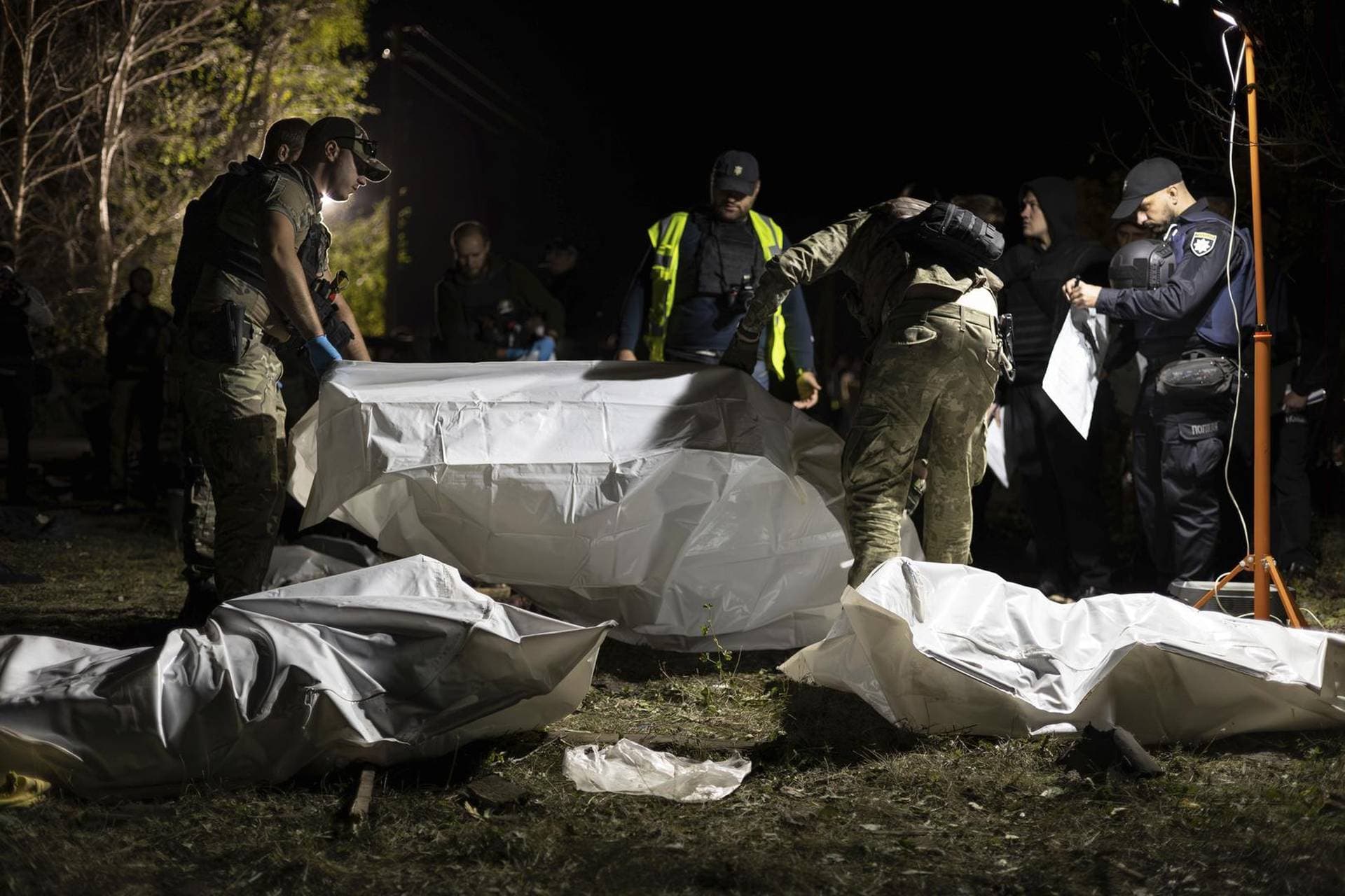 Ukrainian policemen inspect the bodies of persons that were killed by a Russian rocket attack that killed 51 people in the village of Hroza near Kharkiv