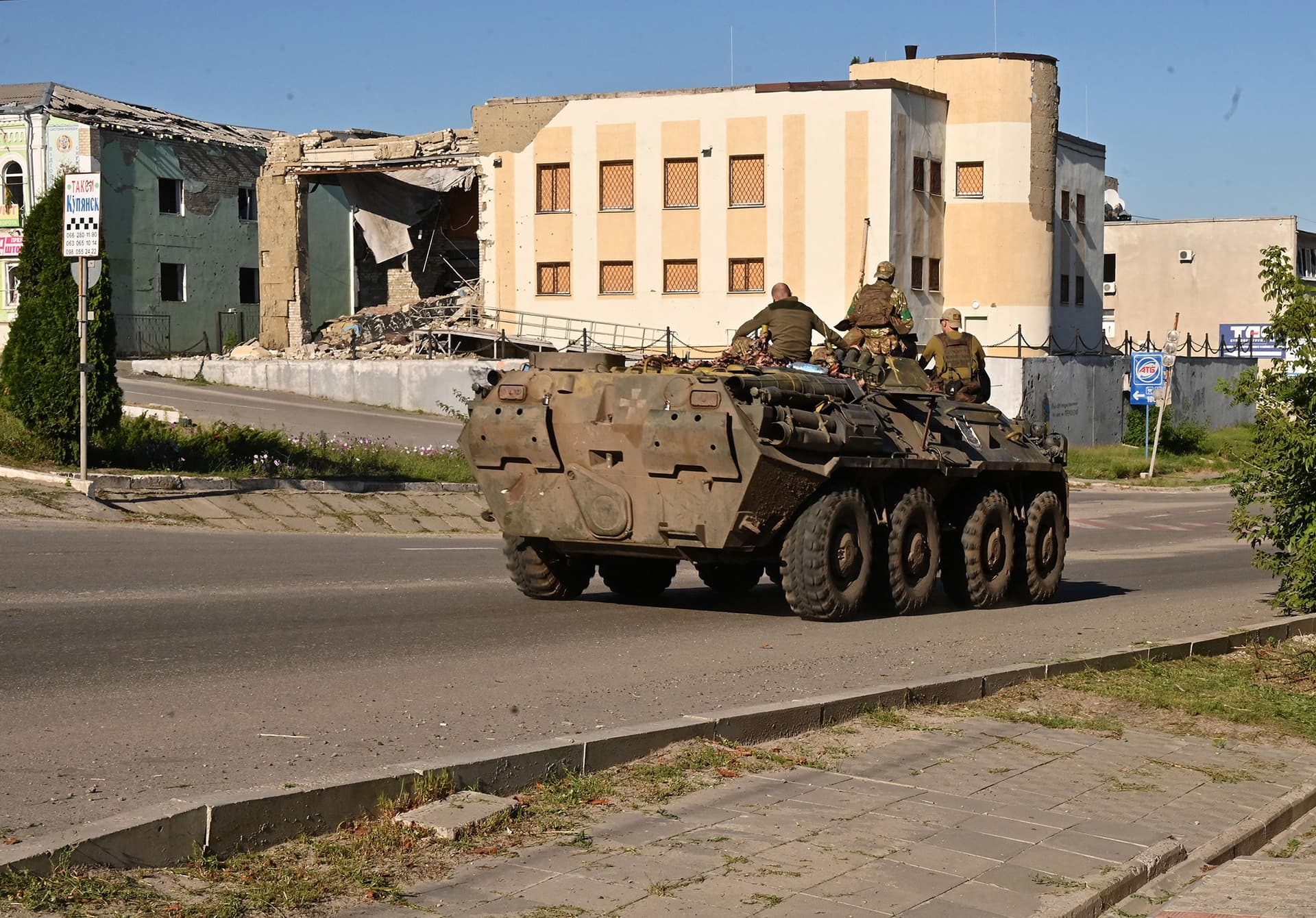 Ukrainian servicemen ride atop of an armored personel carrier past a destroyed building in the town of Kupiansk