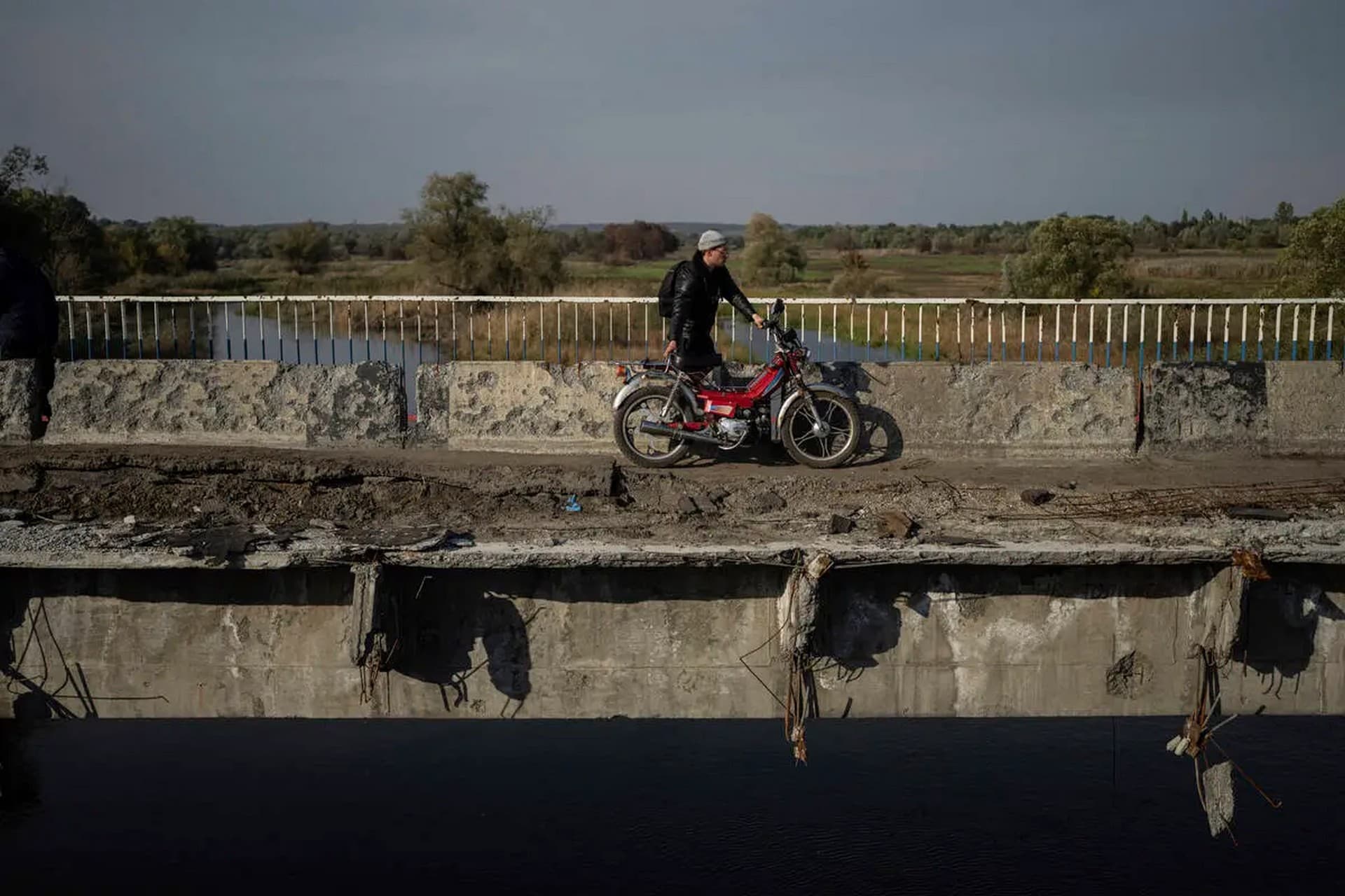 A man hauls his motorbike on a destroyed bridge across Oskil river during evacuation in recently liberated town Kupiansk