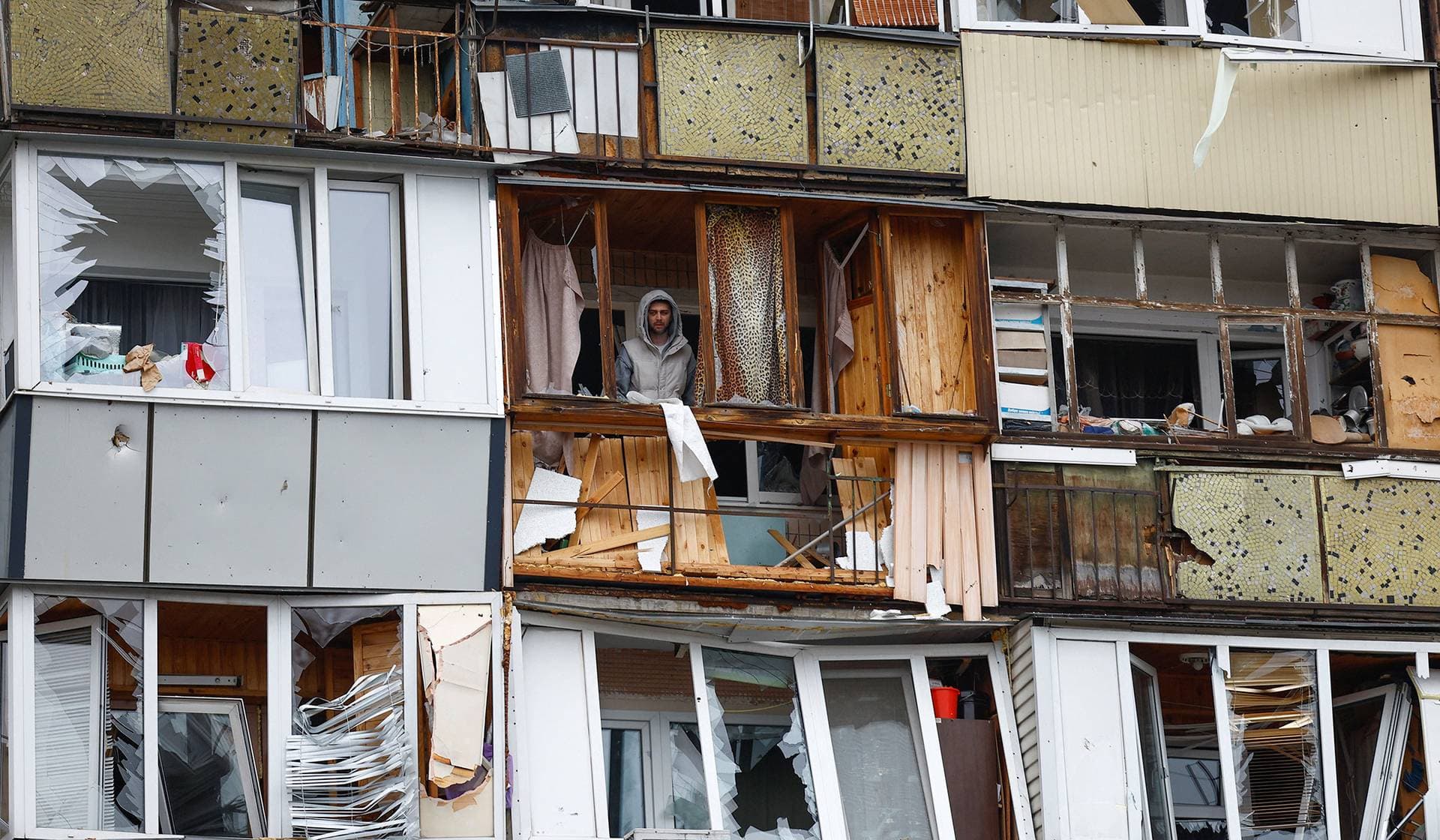 A residents stands on a balcony of his apartment damaged during Russian missile and drone strikes in Kyiv