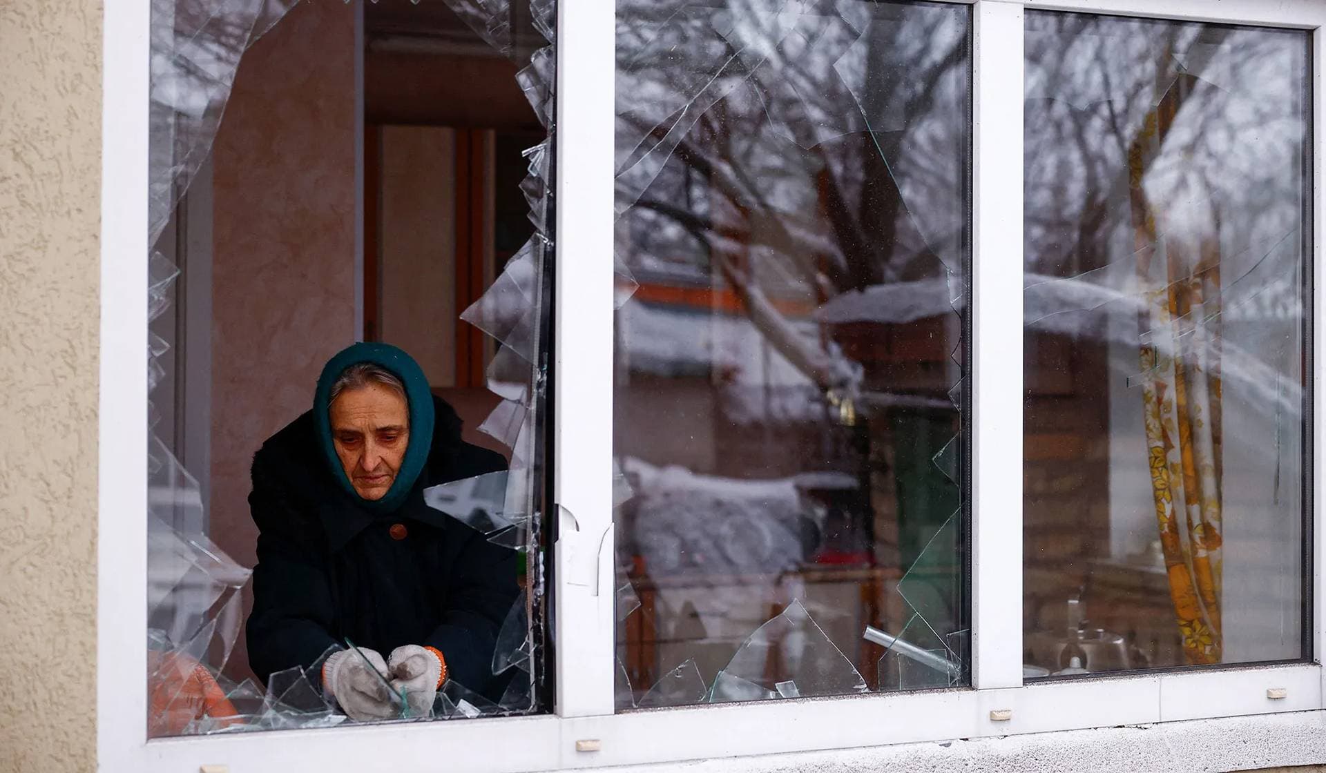 Local resident removes pieces of glass from a broken window of her house damaged by a Russian missile strike in Kyiv