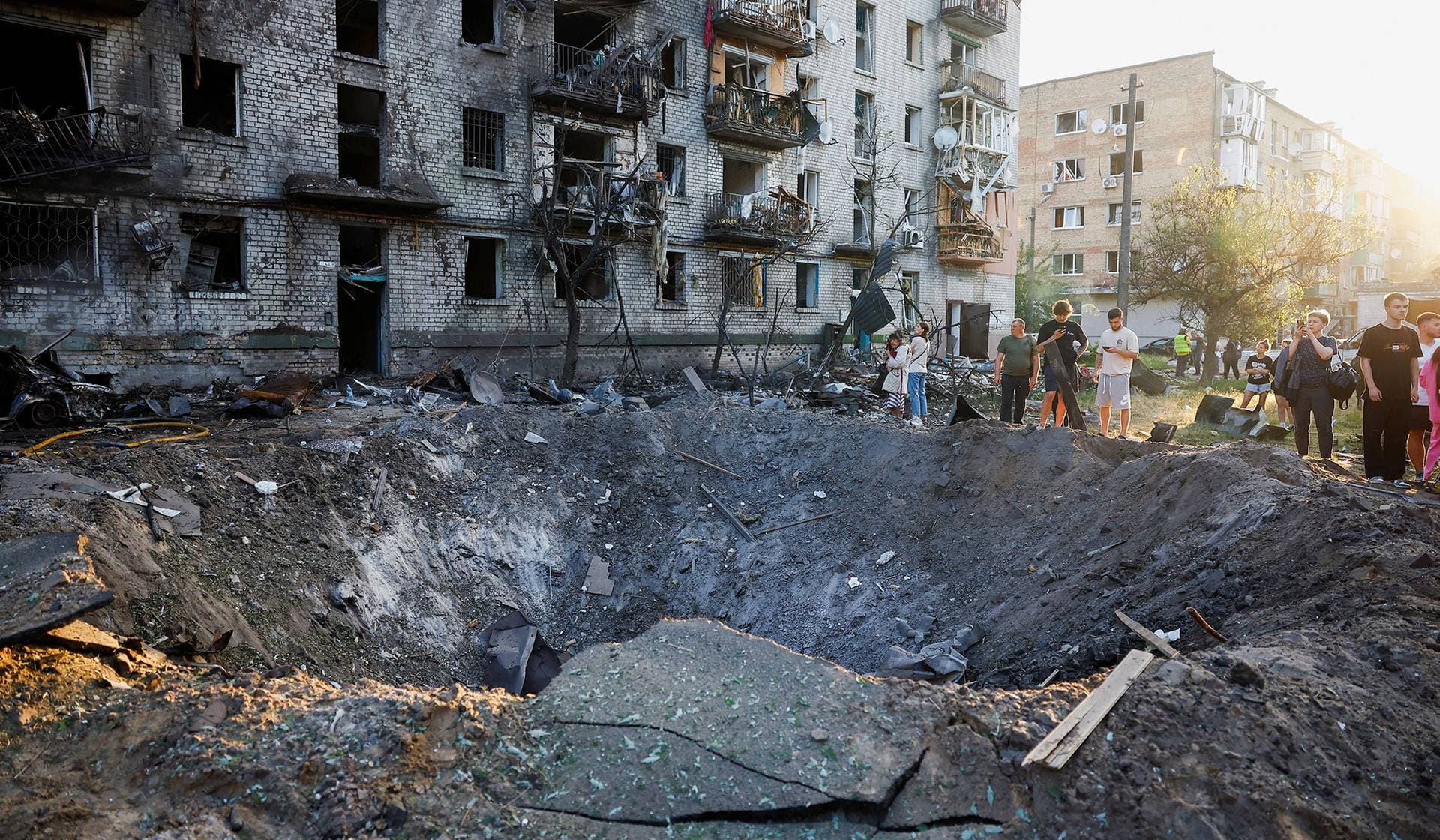Residents stand next to a crater formed at a site during overnight Russian missile and drone strikes in Kyiv