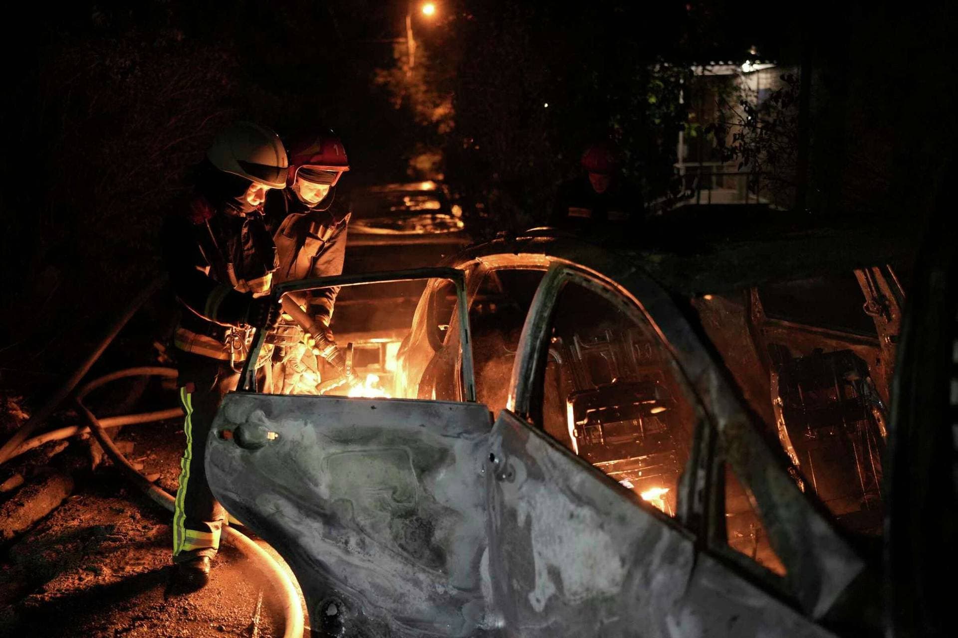 Emergency workers extinguish a fire in a parked car, caused by falling debris from the latest aerial Russian attack in Kyiv