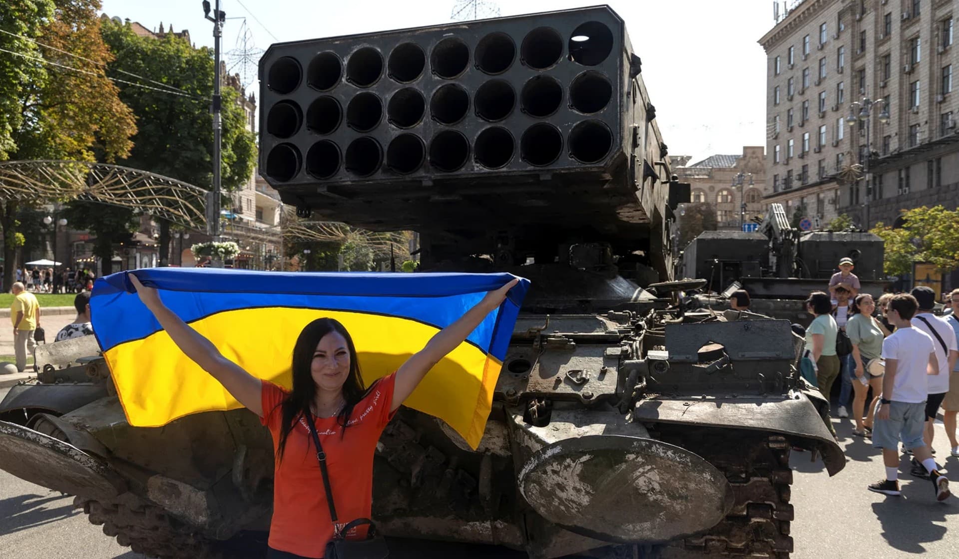 A woman poses for a picture with a national flag on exhibition of destroyed Russian military vehicles and weapons in Kyiv