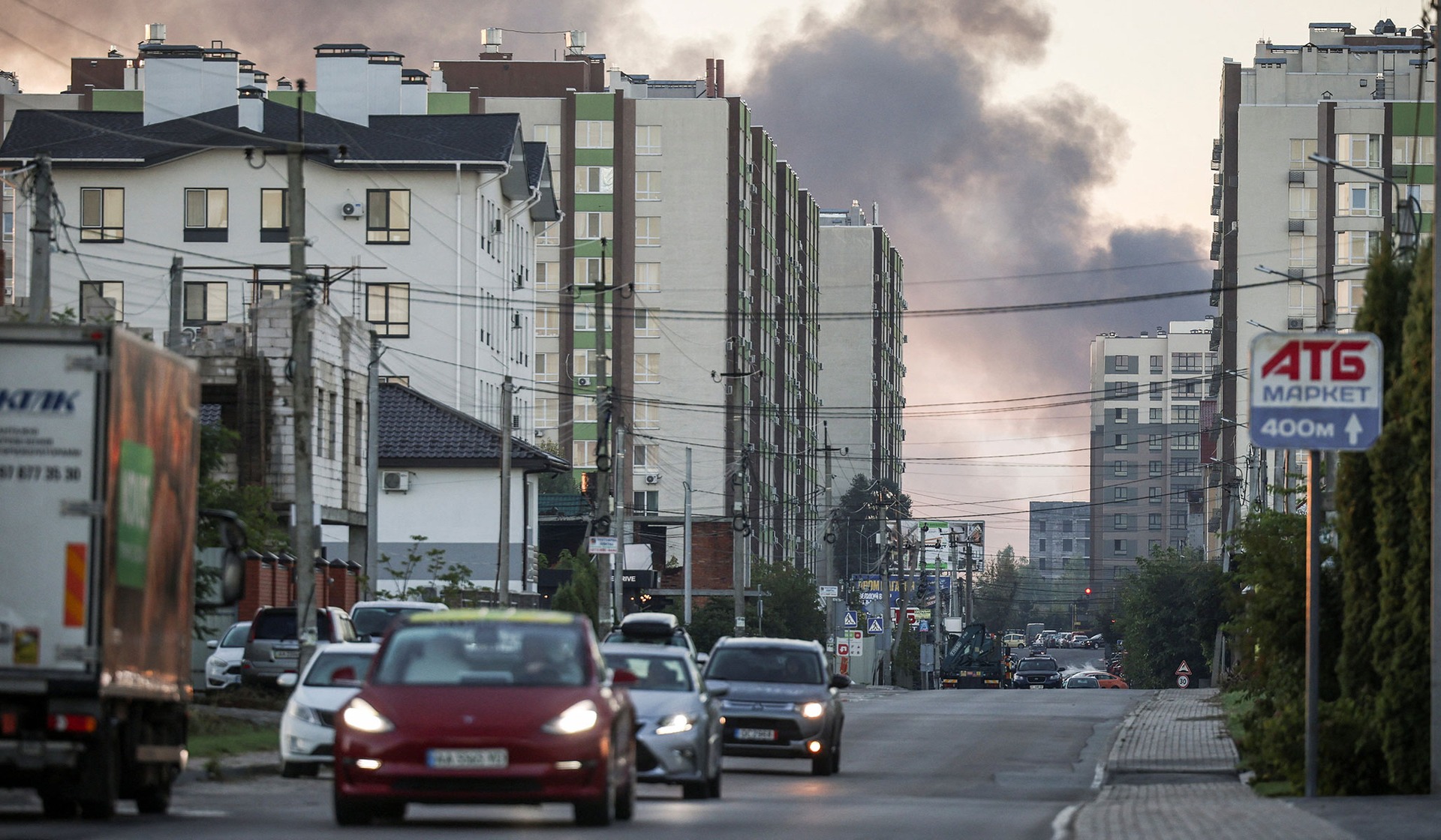 Cars drive along a road in a residential area as smoke rises in the background following a Russian drone strike in Kyiv Region, Ukraine, September 23, 2026.