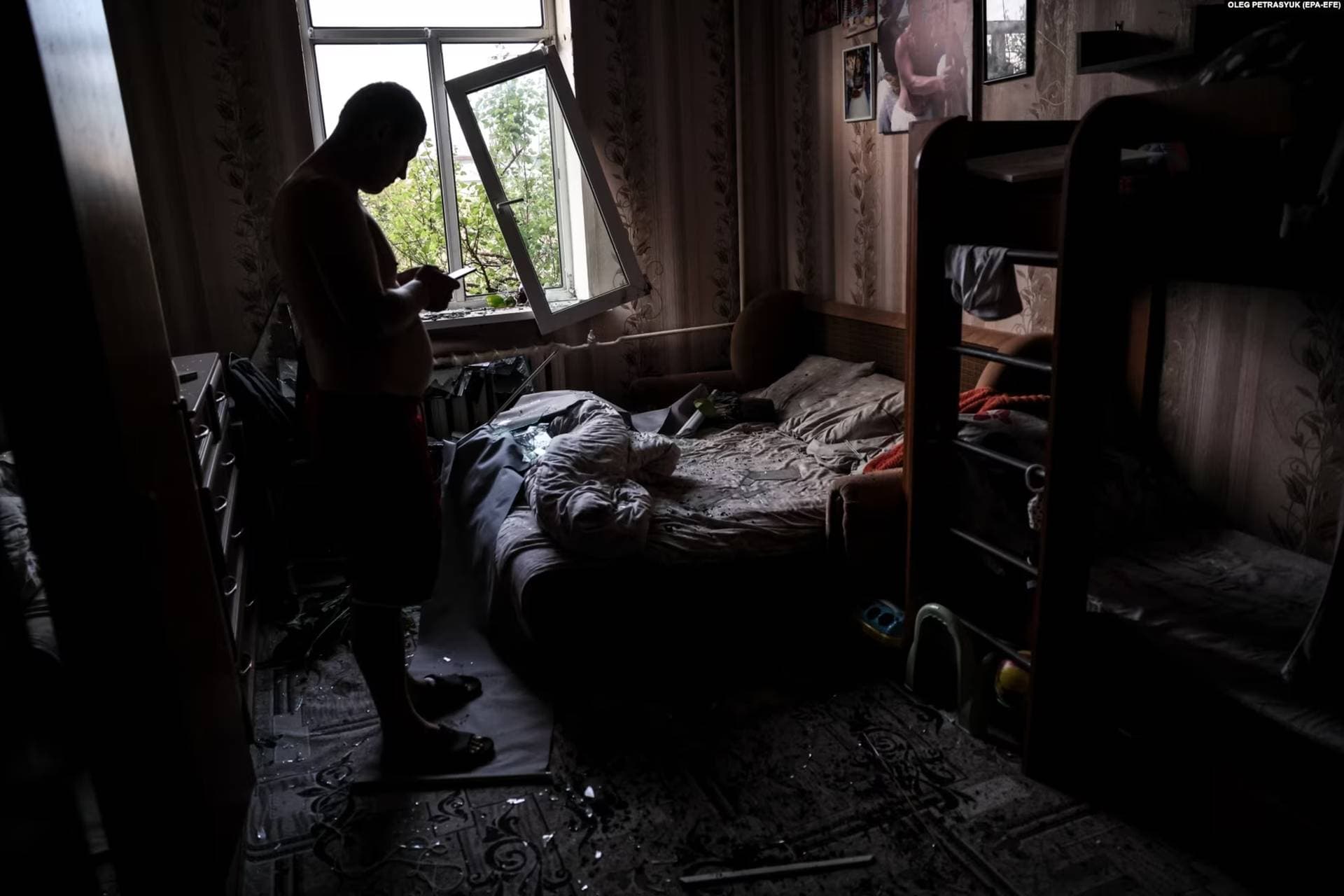 Kyiv resident checks his phone after surveying the damage inside his flat