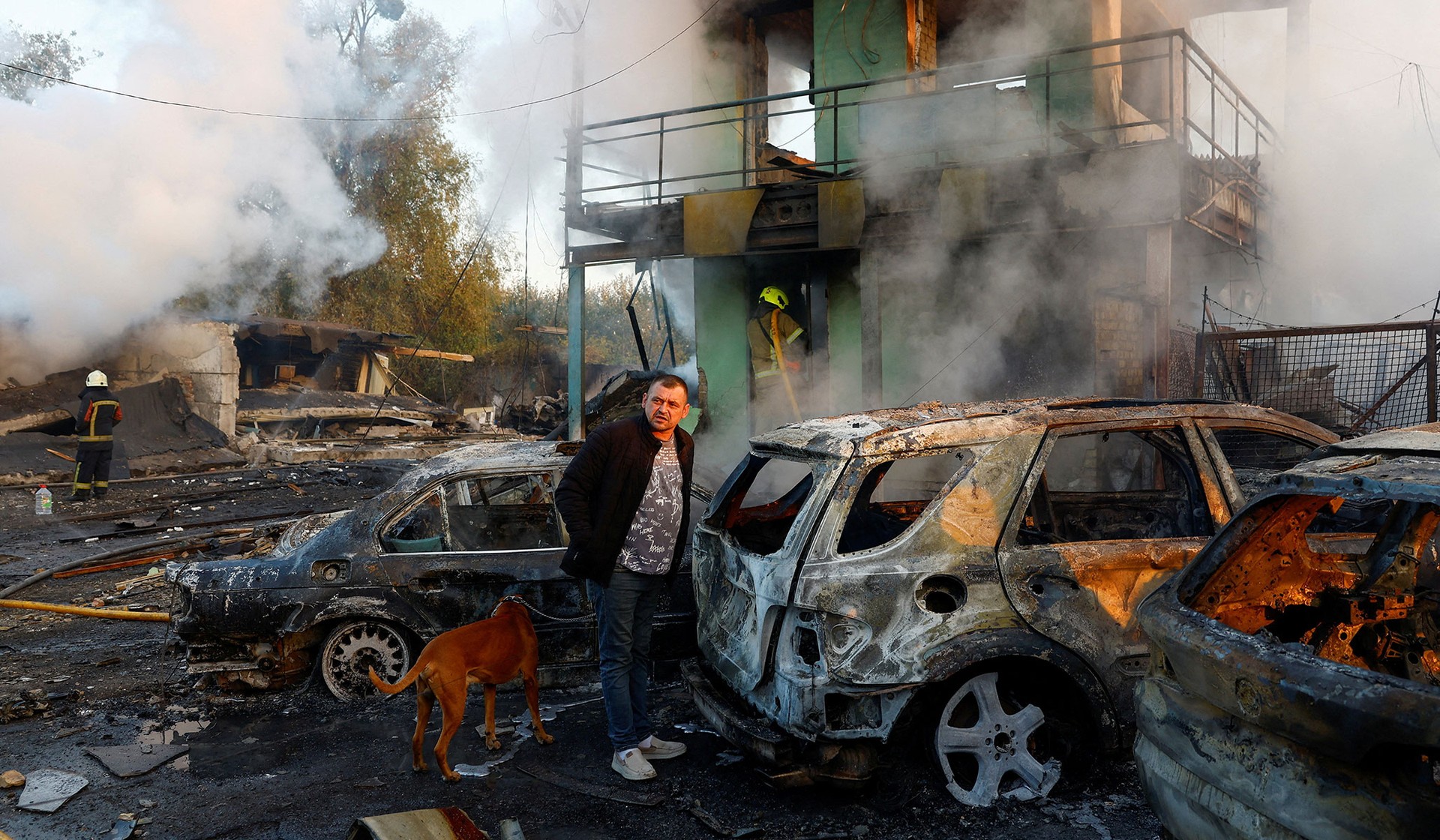 A resident with a dog looks on at the site of private car garages hit by a Russian missile strike in Kyiv