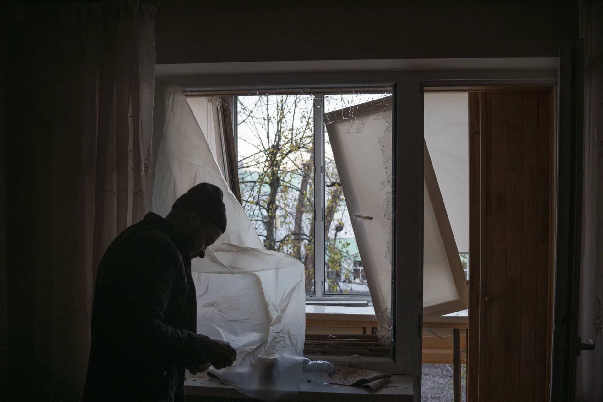A man uses plastic to cover a broken window in his apartment following a Russian drone attack in Kyiv