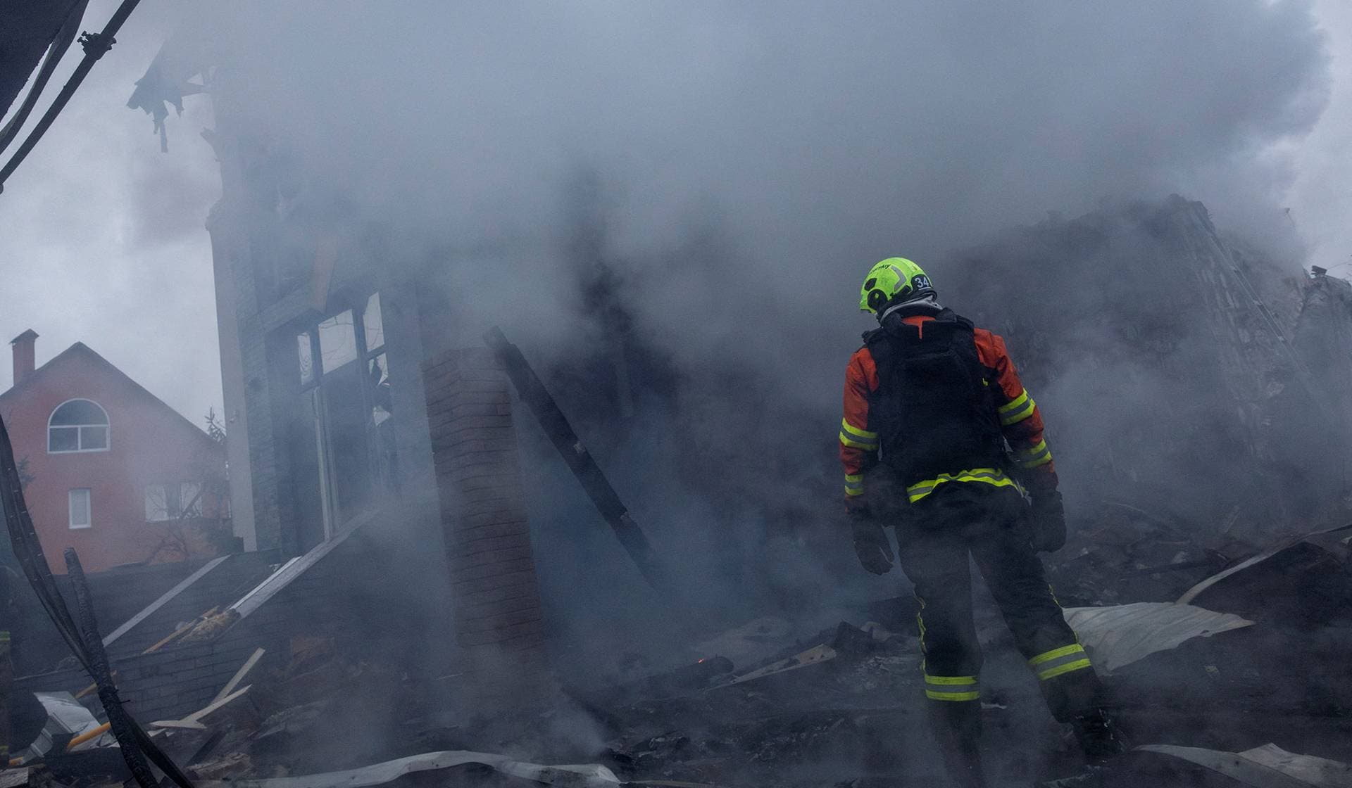A firefighter stands at the site of a private home that went up in flames after it was hit by a Russian drone during a night of attacks on Kyiv