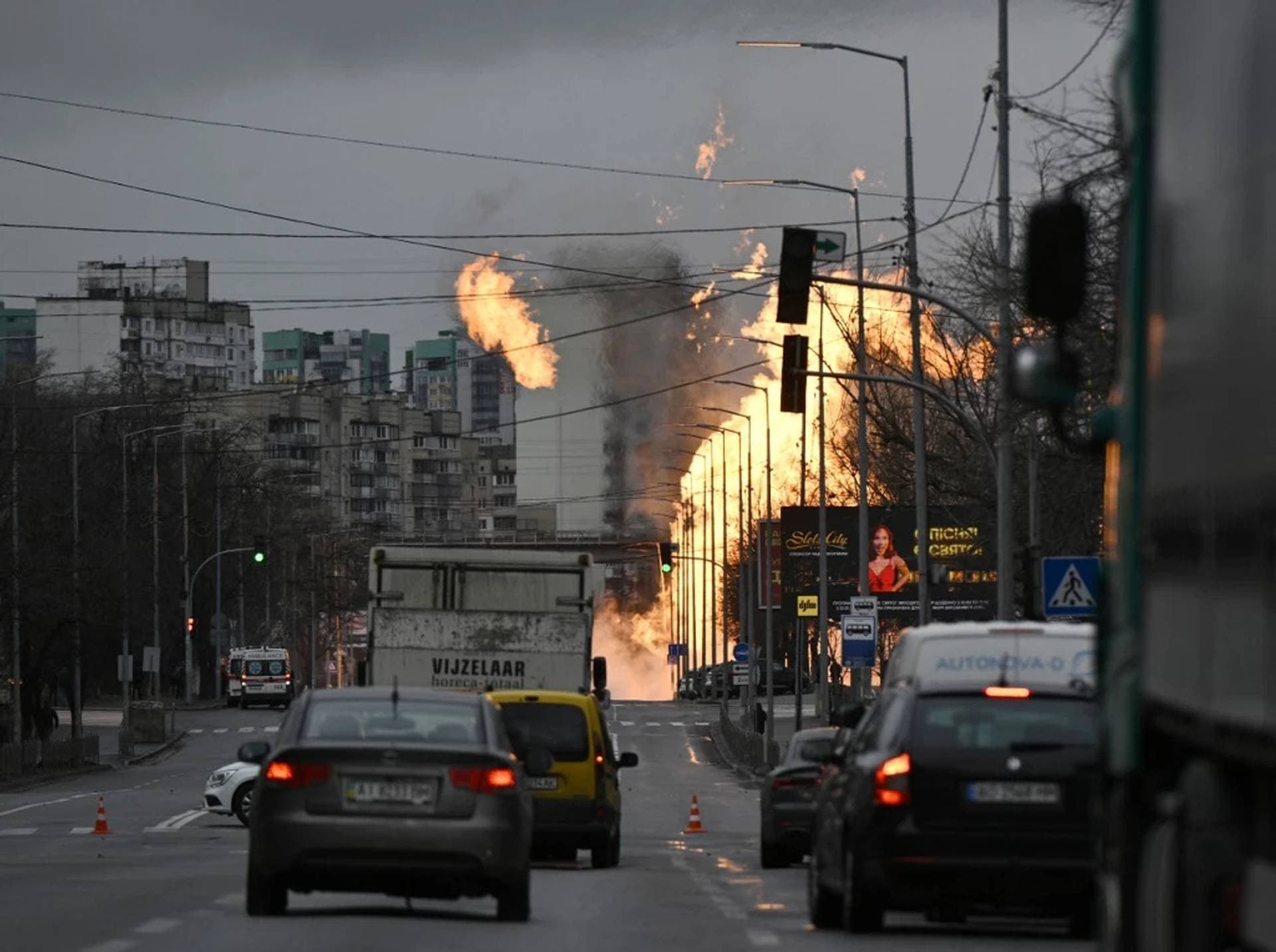 Motorists drive their cars on a road as Ukrainian firefighters attempt to extinguish a fire after a missile strike in Kyiv