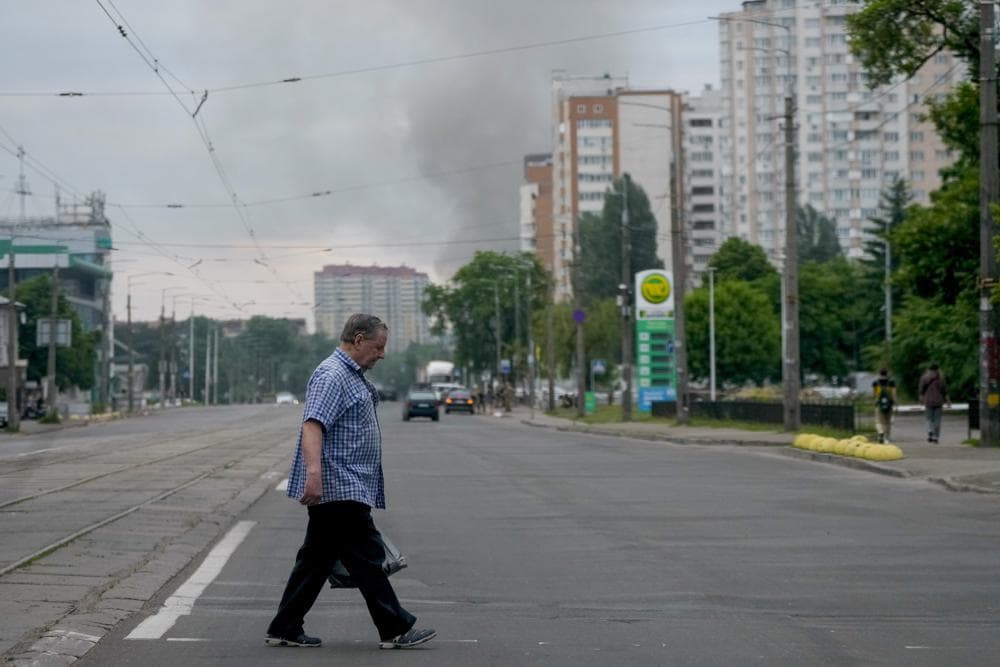 A man crosses a street as smoke rises in the background after Russian missile strikes in Kyiv