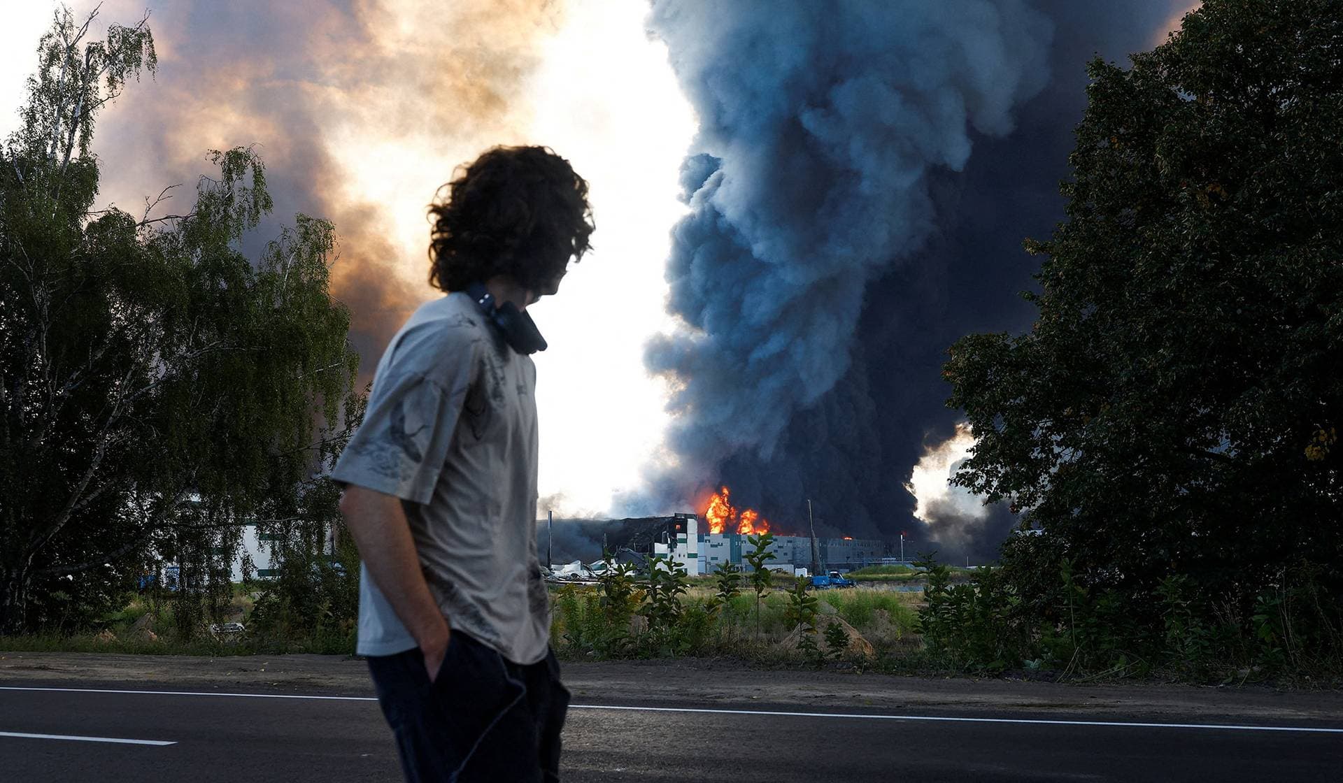 A man looks on as smoke rises over a warehouse, which was hit by a Russian drone strike in Kyiv Region