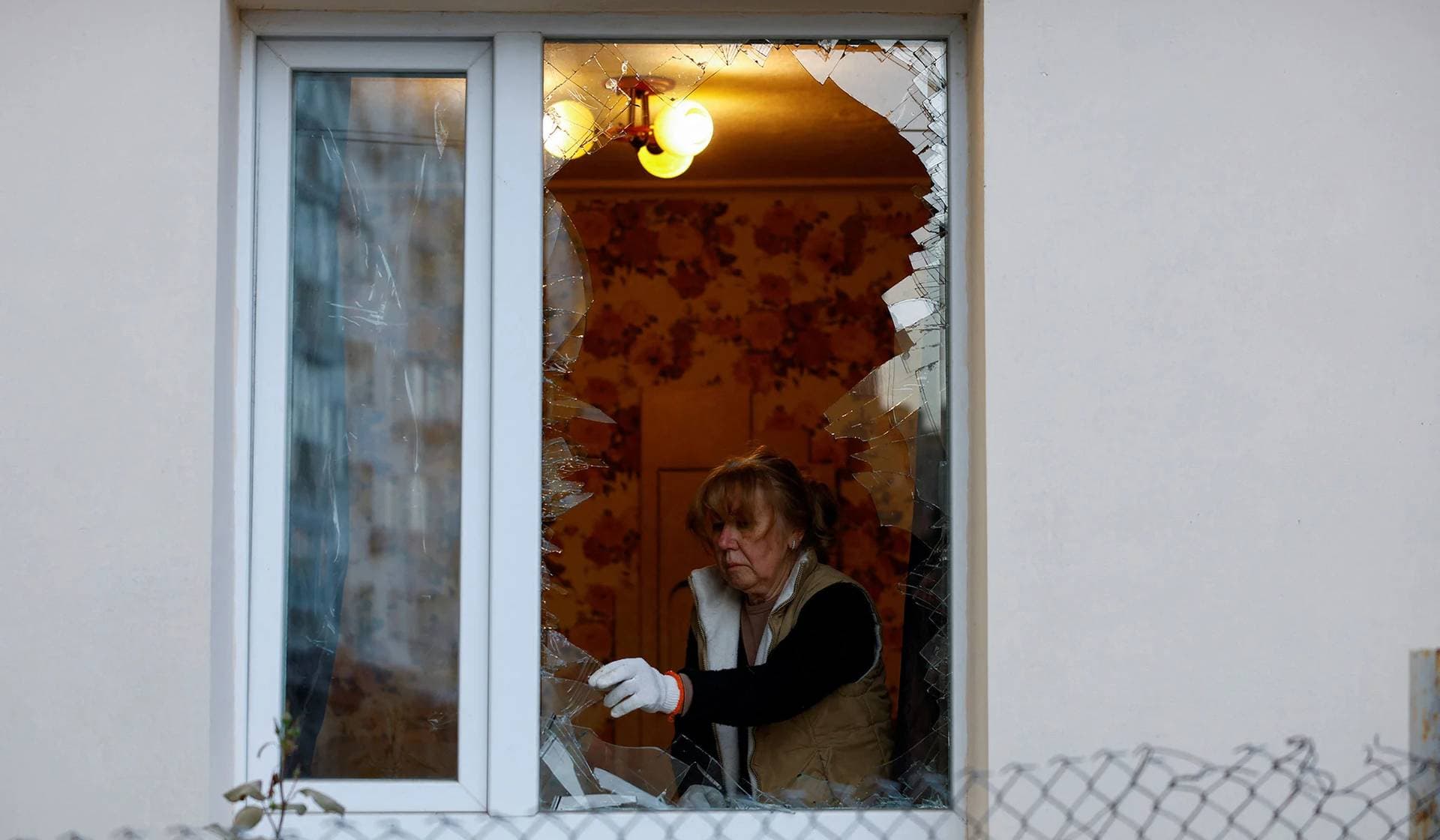 A person removes shards of glass from a window after a massive Russian drone strike in Kyiv