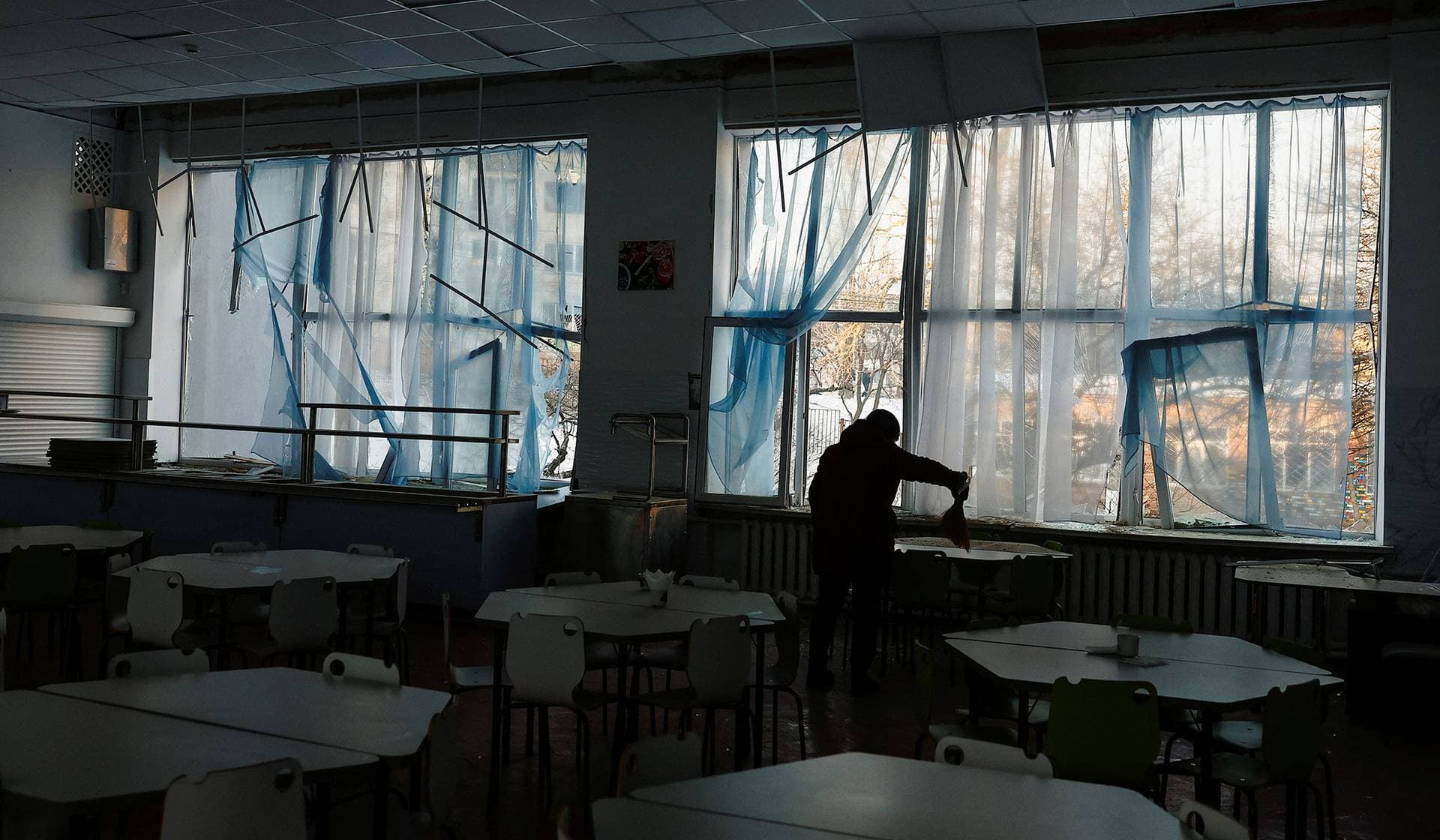 An employee of the school cleans up inside a school building that was damaged on an apartment building near the school in Kyiv