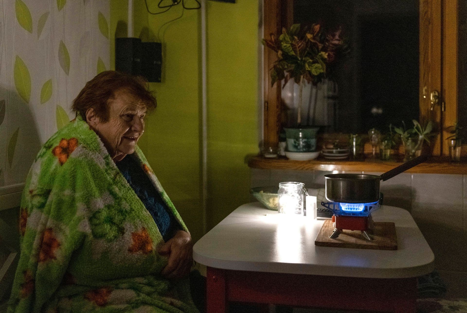 An elderly woman cooks food on a gas burner during a blackout in Kyiv