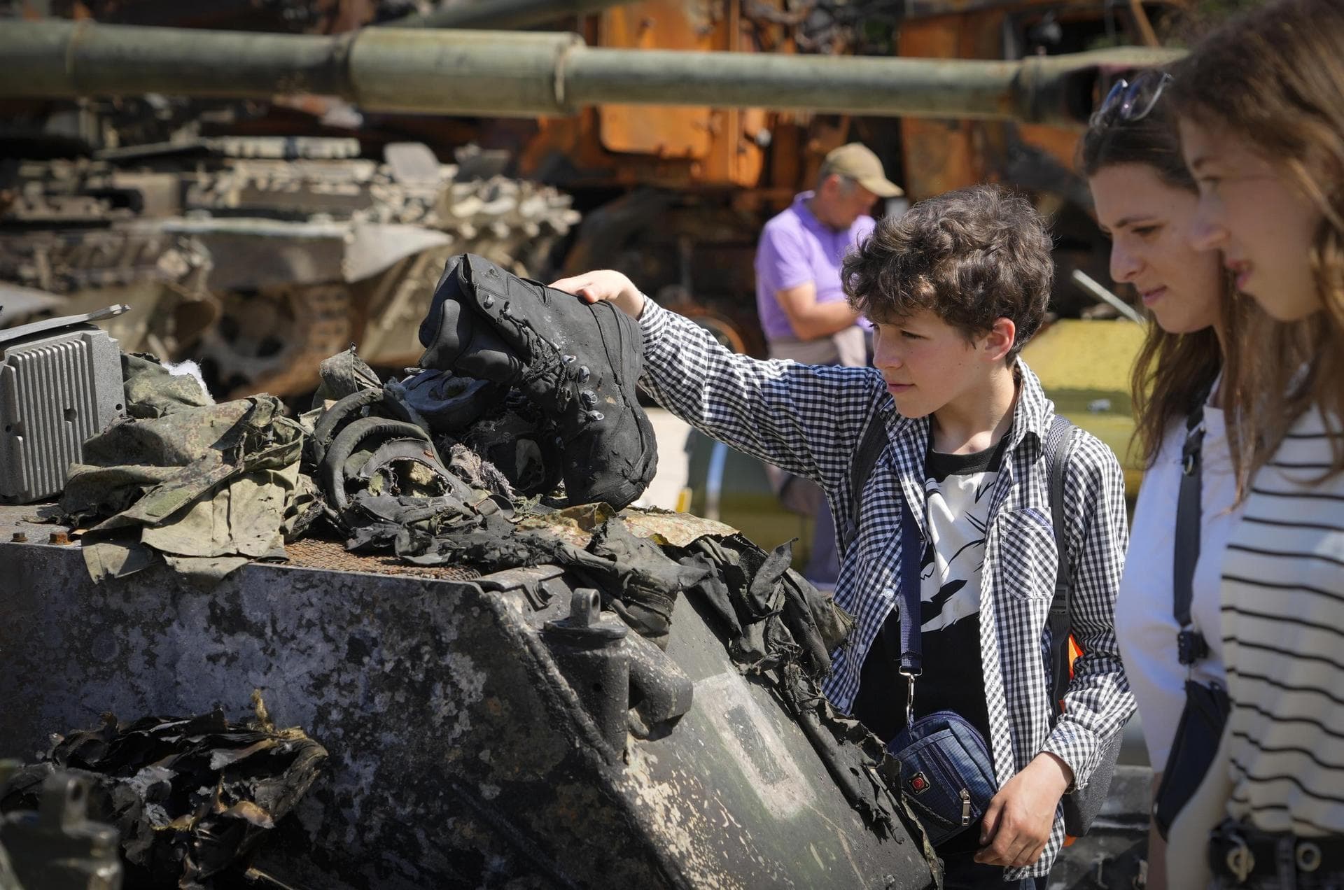 A boy holds a boot of a killed Russian soldier at a destroyed Russian tank installed as a symbol of war in central Kyiv