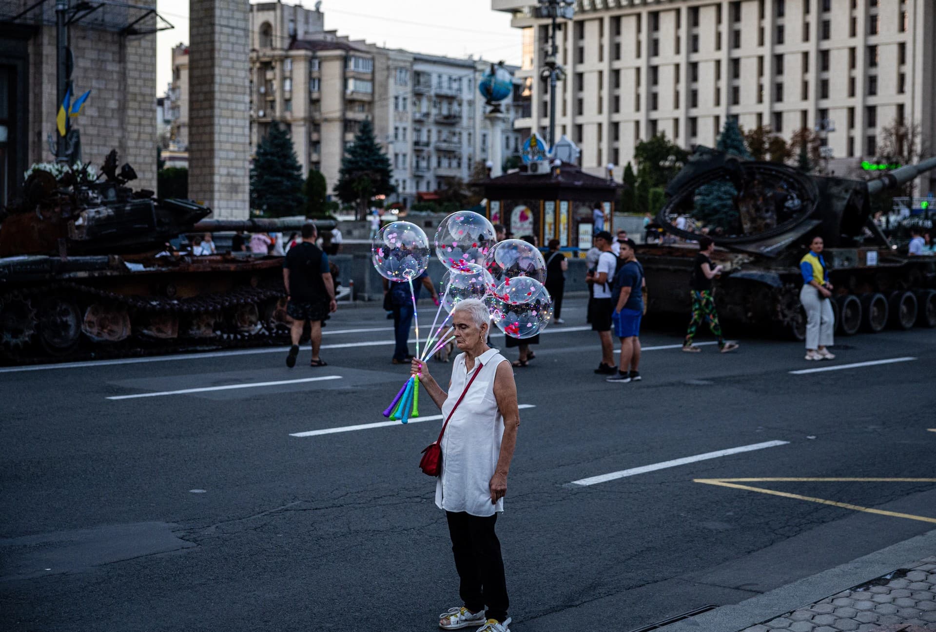 An elderly woman sells glowing balloons next to destroyed Russian military equipment in Kyiv