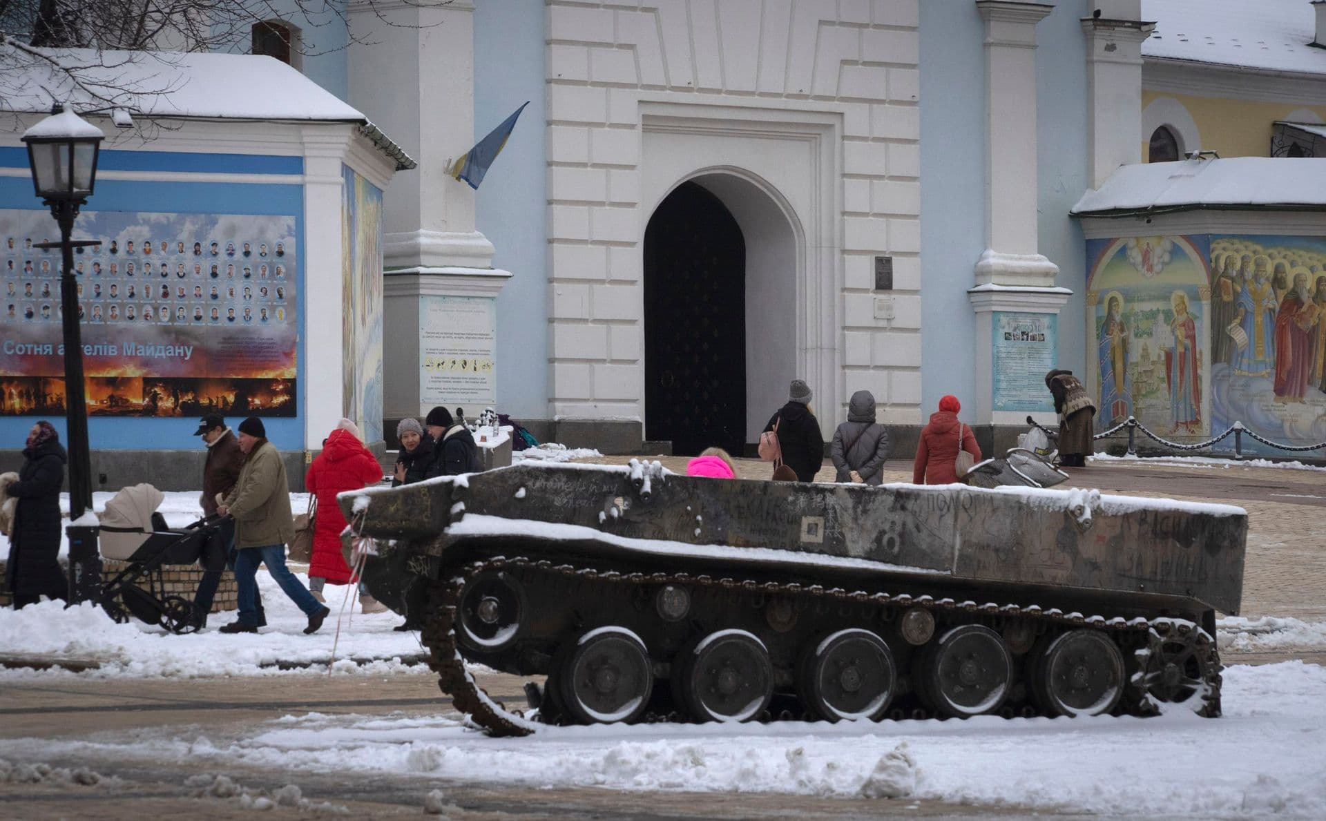 People pass by the entrance to St.Michael Cathedral, with a damaged Russian military vehicle in the foreground, in central Kyiv