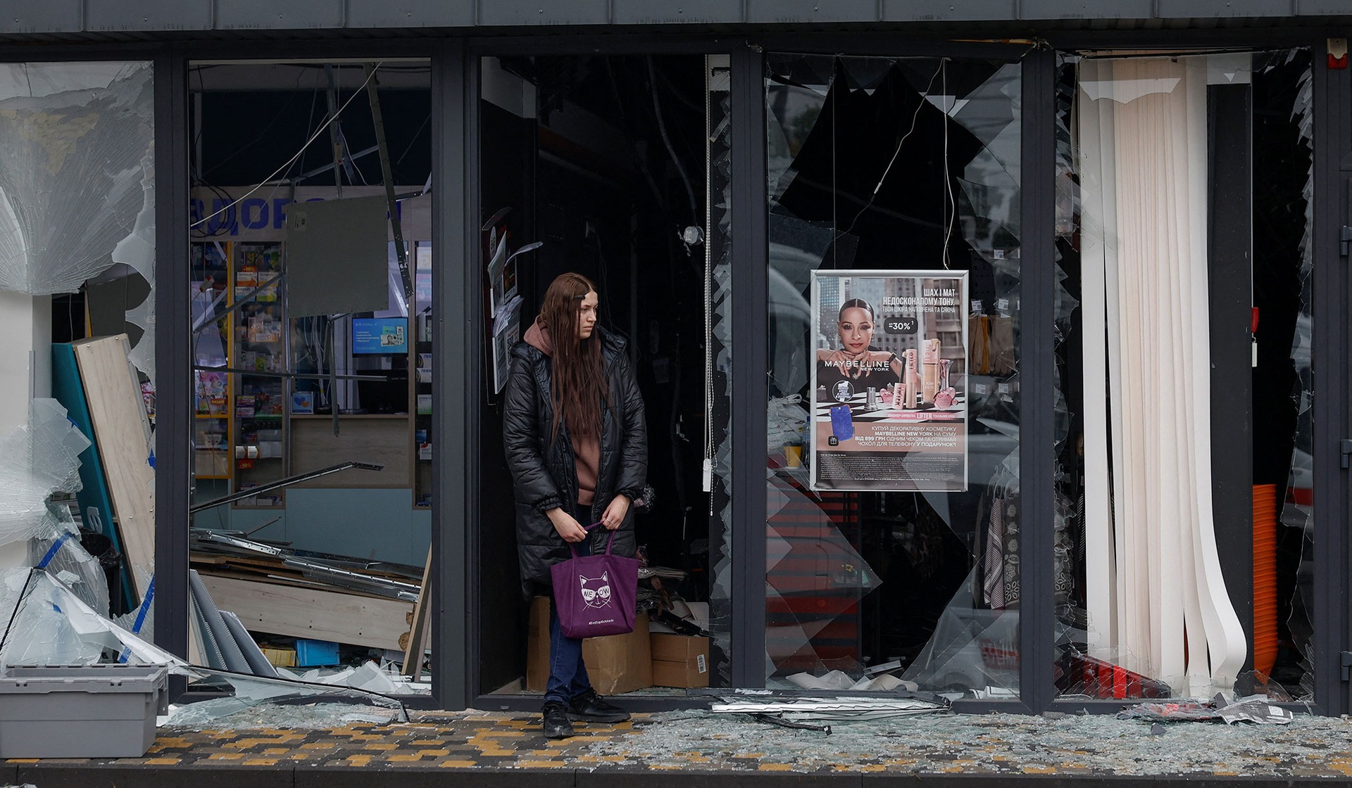 A woman stands next to a damaged beauty store near a metro station in Kyiv