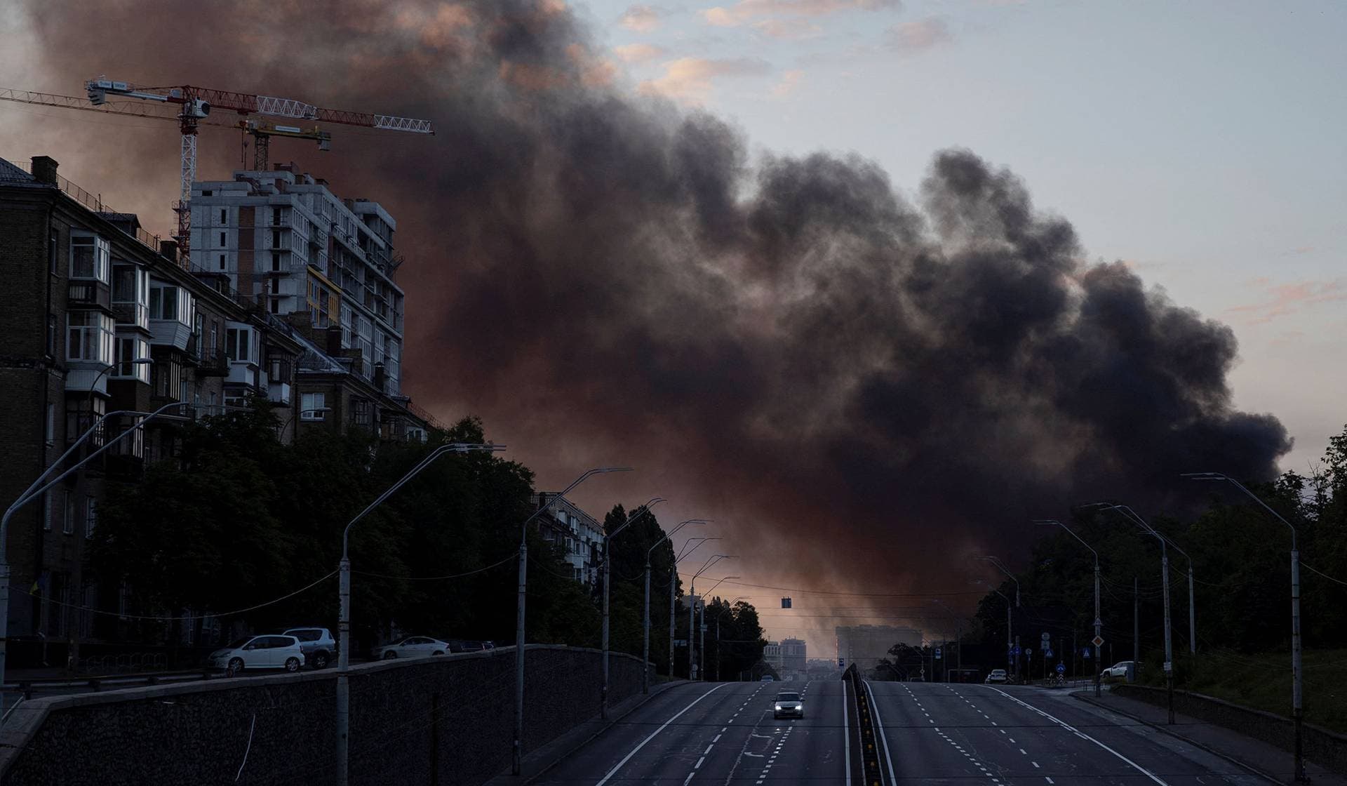 A column of smoke rises over the city as a car drives on a highway following Russian missile strikes in Kyiv