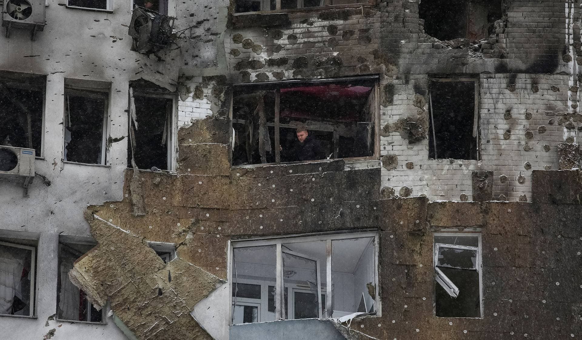 A resident stands on a balcony of his apartment damaged during Russian drone strike in Kyiv