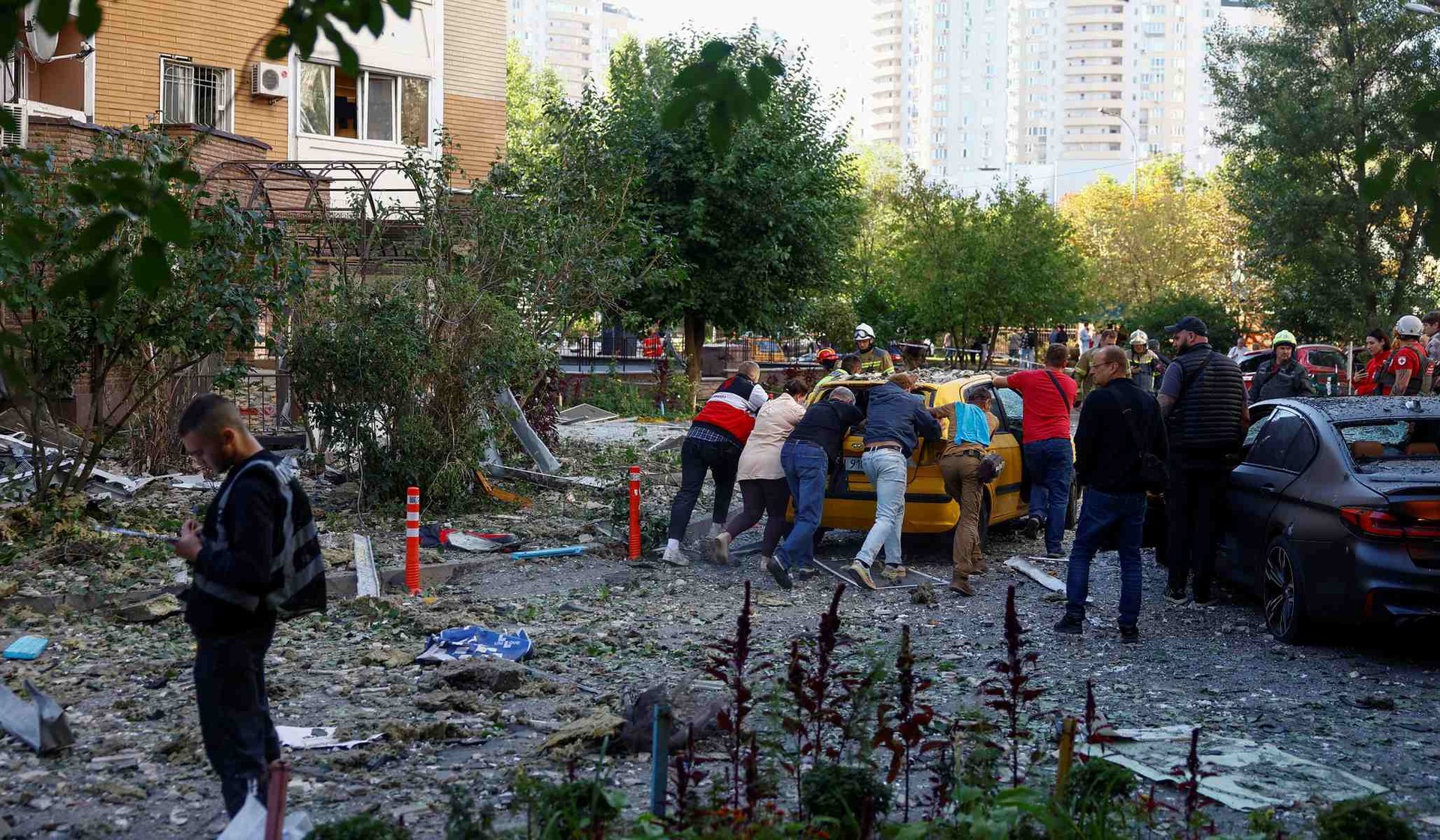 People push a damaged car from the site of a Russian drone strike on an apartment building in Kyiv