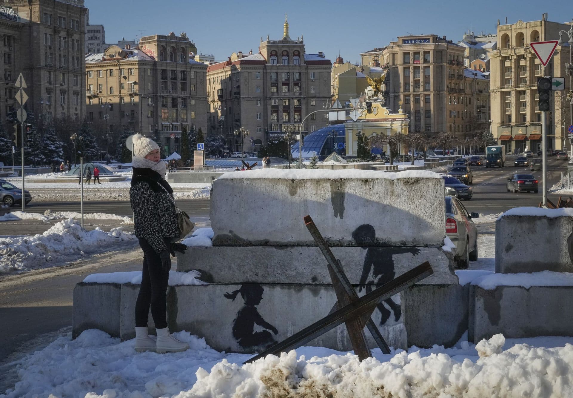 A woman stands next to a picture with an artwork on concrete blocks in the main square in Kyiv