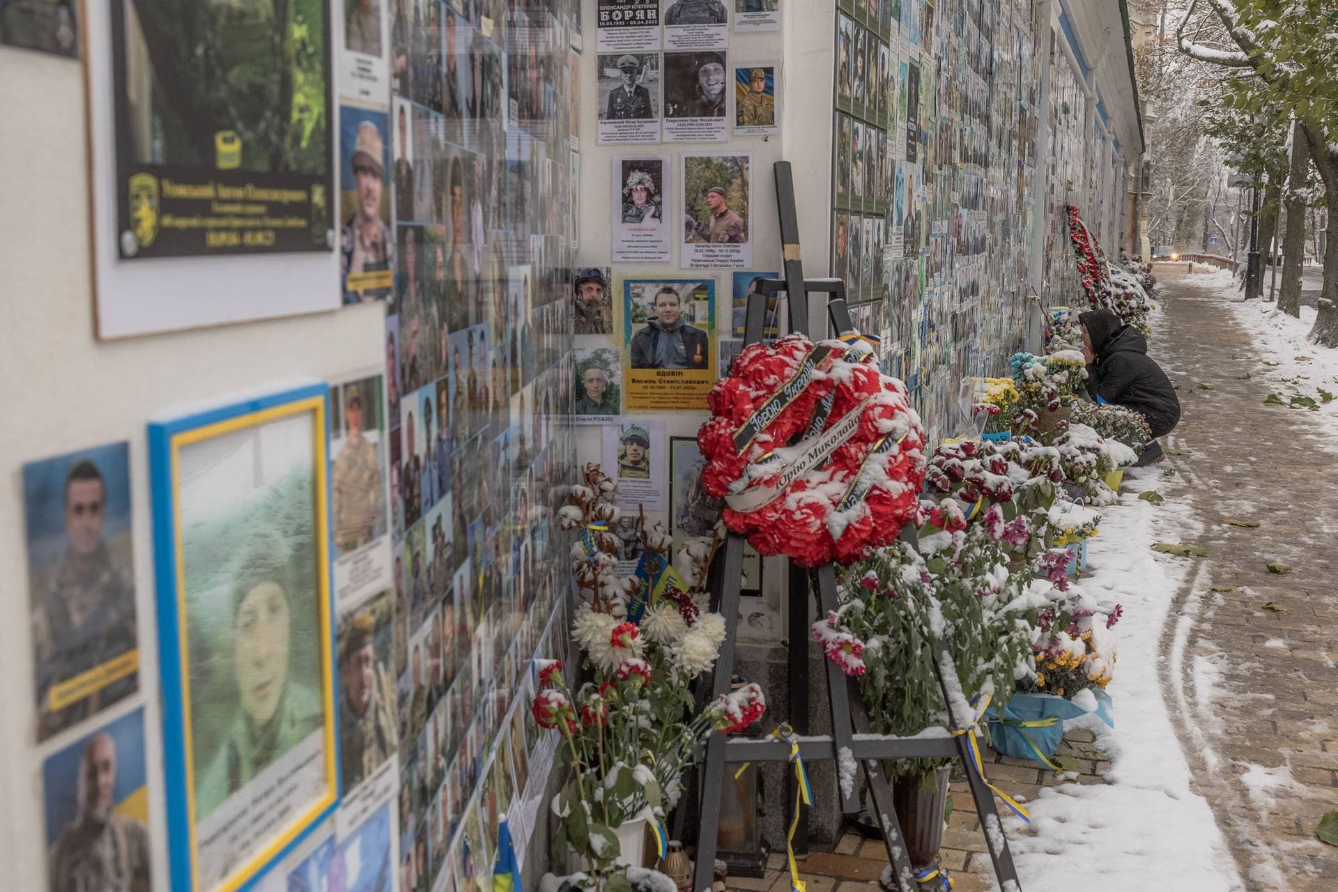 A woman sits in a street in front of the memorial wall of fallen defenders of Ukraine in Kyiv