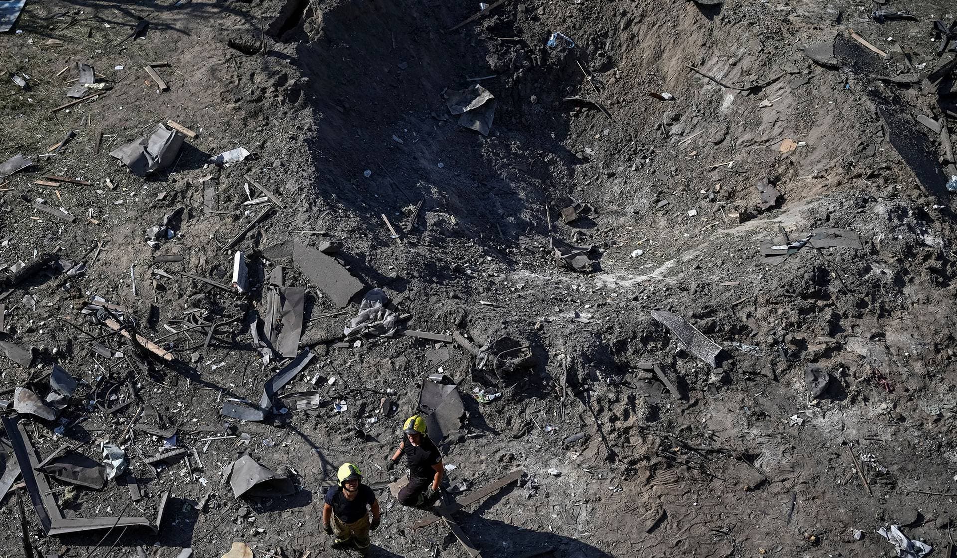 Rescuers stand next to a crater formed at a site during overnight Russian missile and drone strikes in Kyiv