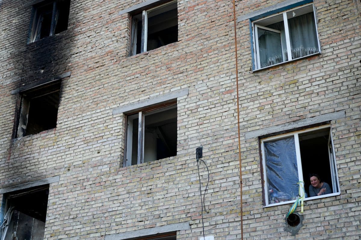 A woman looks outside her window at a building destroyed by attacks in Gorenka