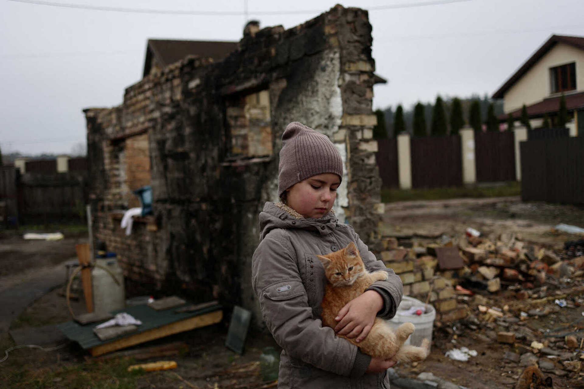 a 9-year-old Ukrainian girl holds her cat outside her half-sister's destroyed house in the village of Moshchun