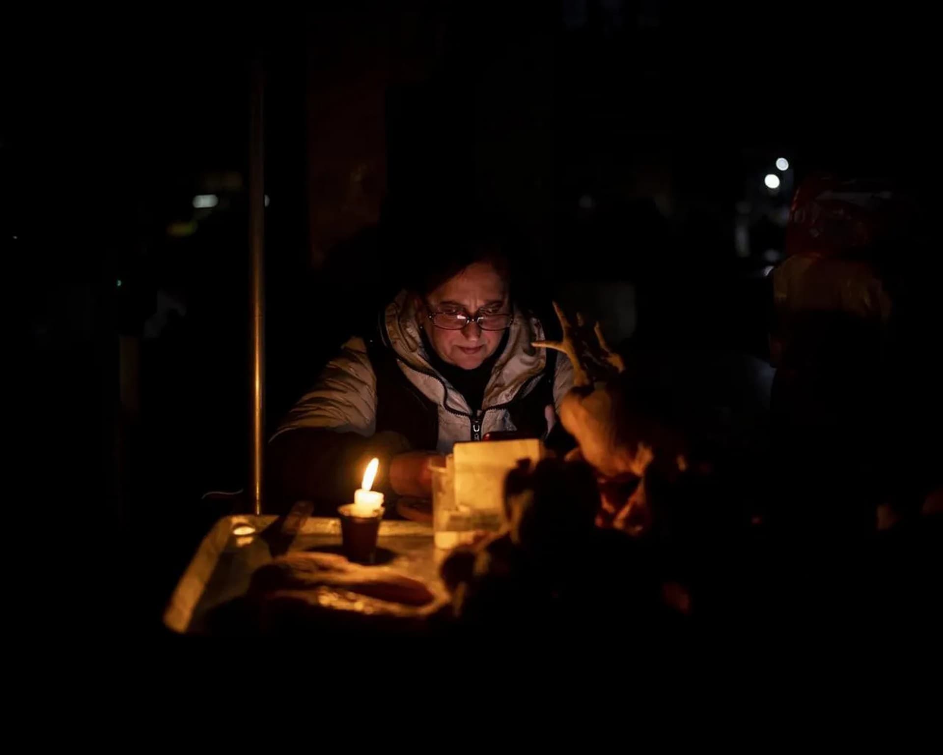 A meat vendor uses a candle to illuminate her market meat stall during a power outage in Kyiv